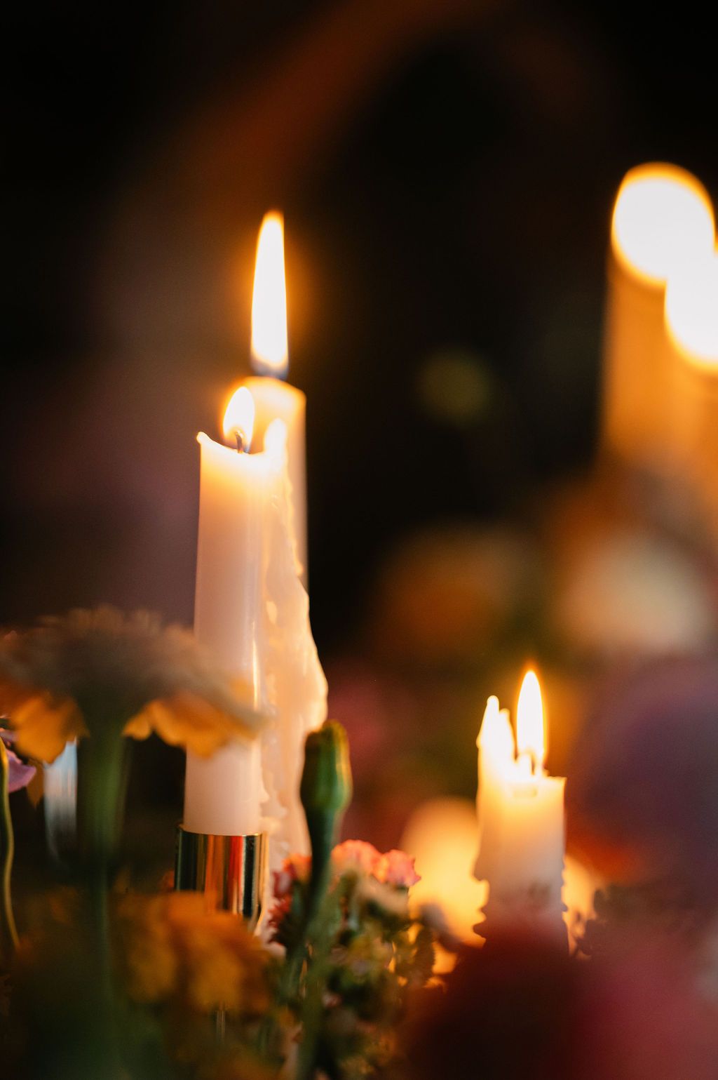 Burning white candles create a warm glow against a dark background in a romantic setting.