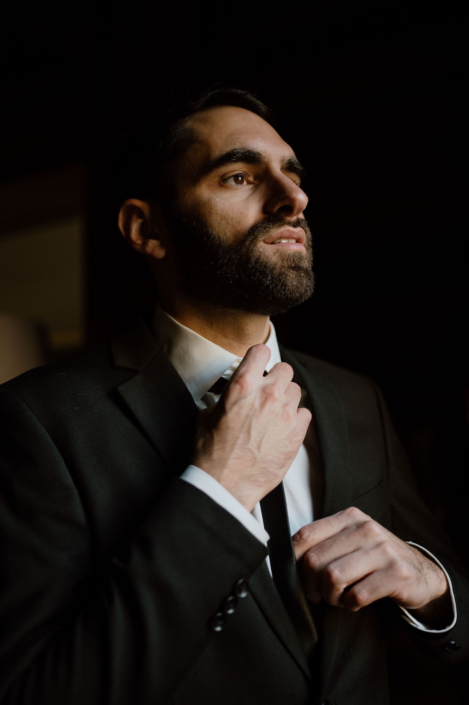 Artistic portrait of a well-dressed person adjusting their tie in dramatic lighting.