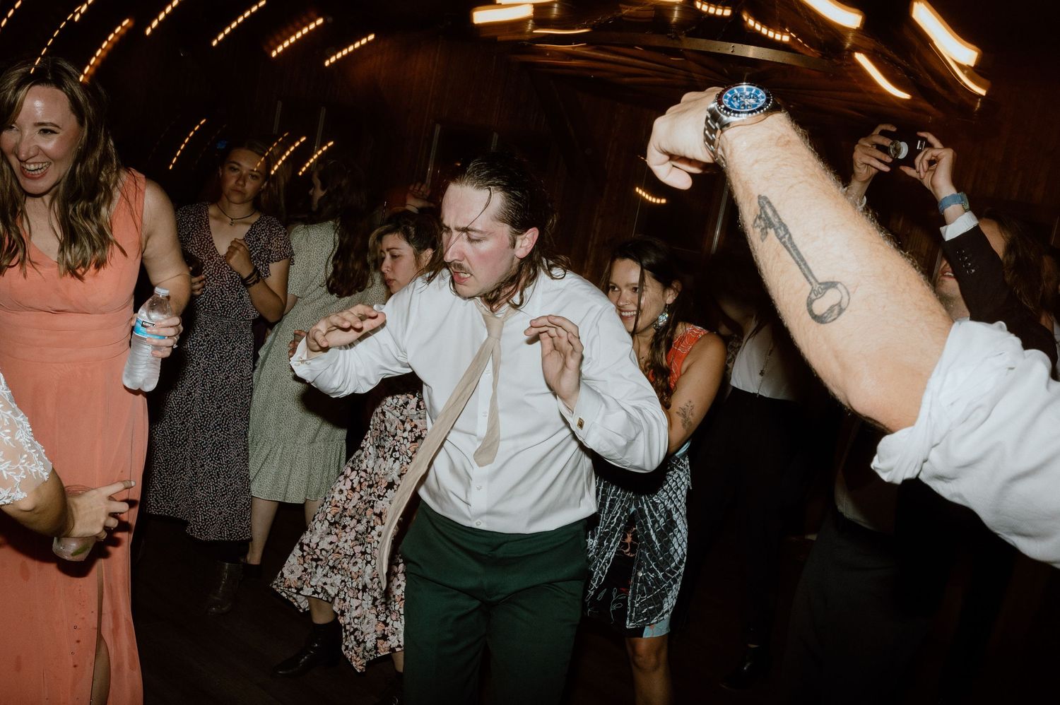 Energetic dancing and celebration at a dimly lit wedding reception venue.