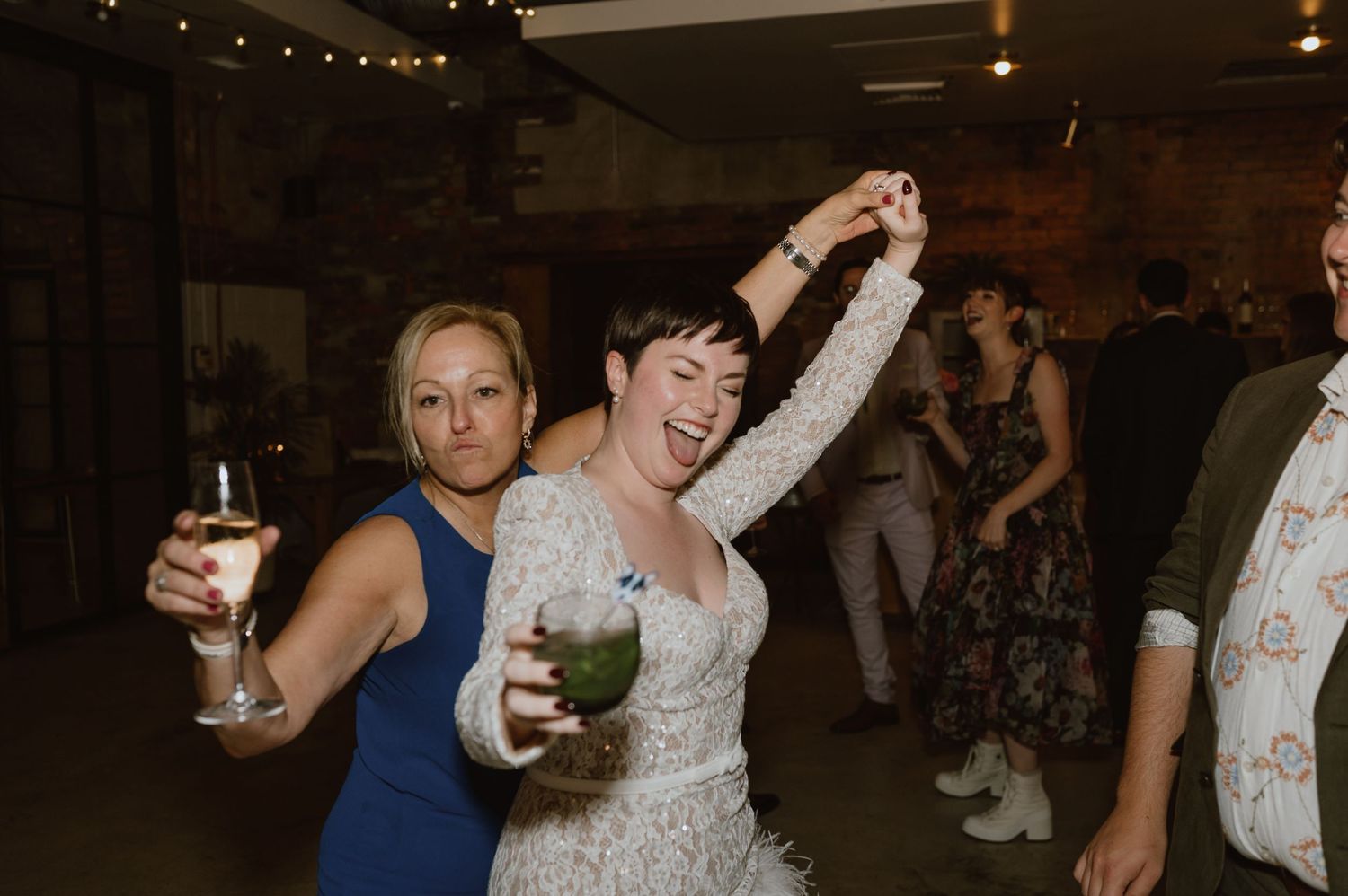 Wedding guests dancing and holding cocktails at an industrial-style reception venue.