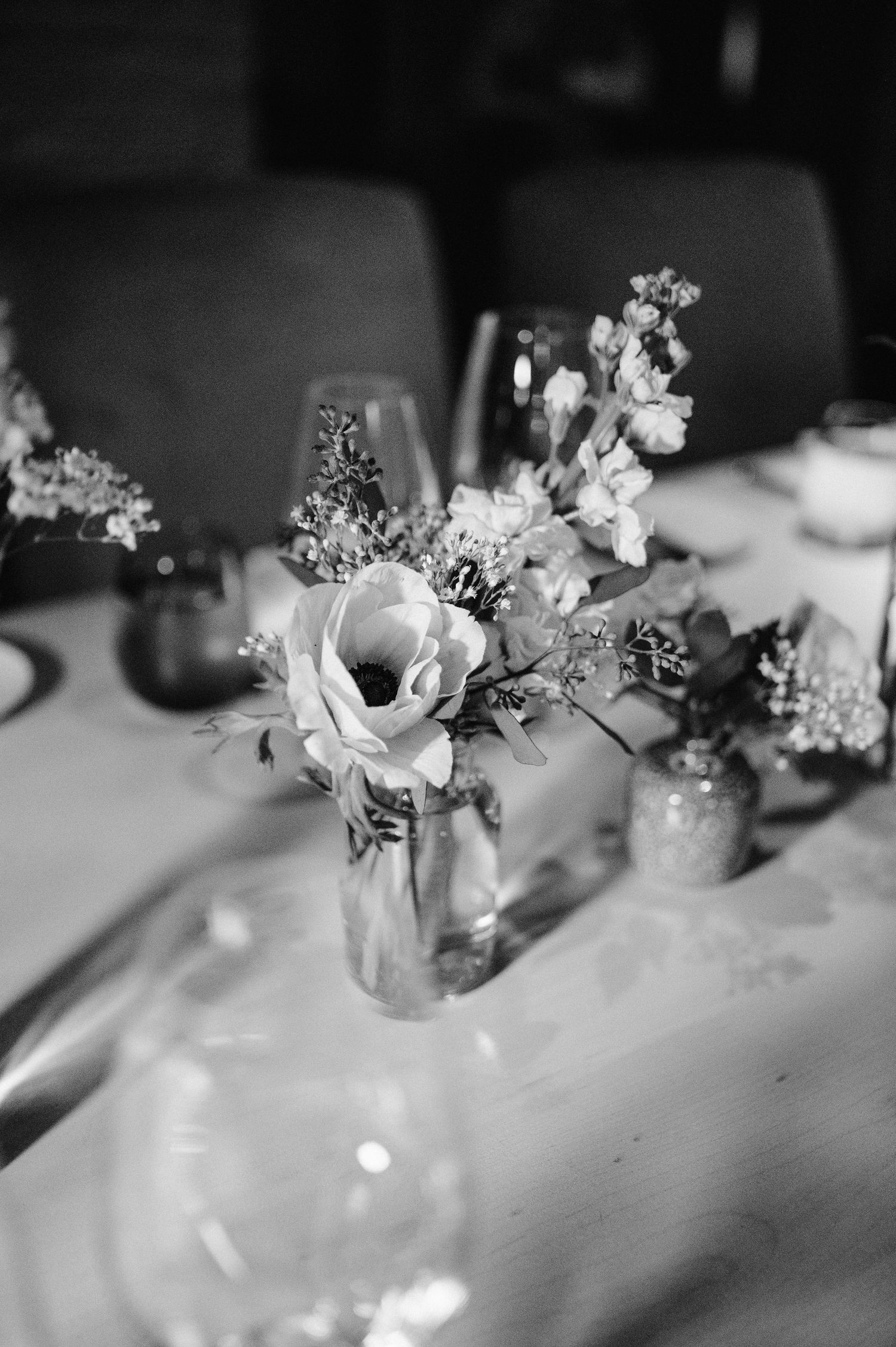 Black and white image of delicate floral centerpiece in glass vase on white tablecloth.