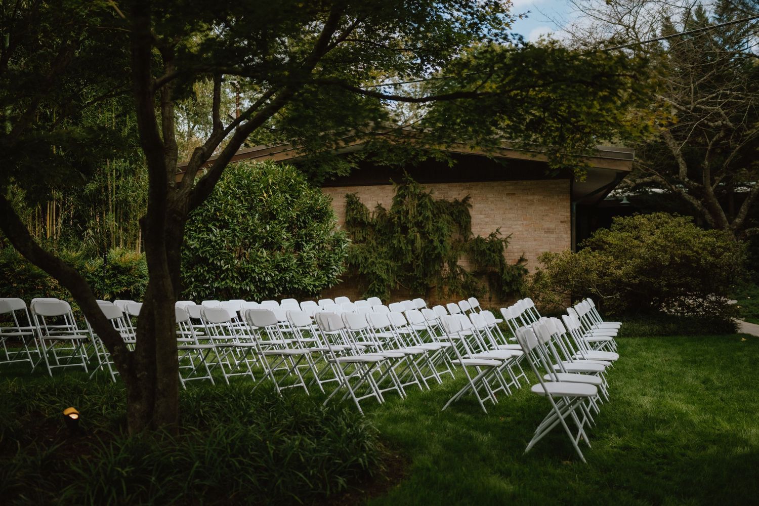 White folding chairs arranged in rows on a lawn for an outdoor ceremony under shaded trees.