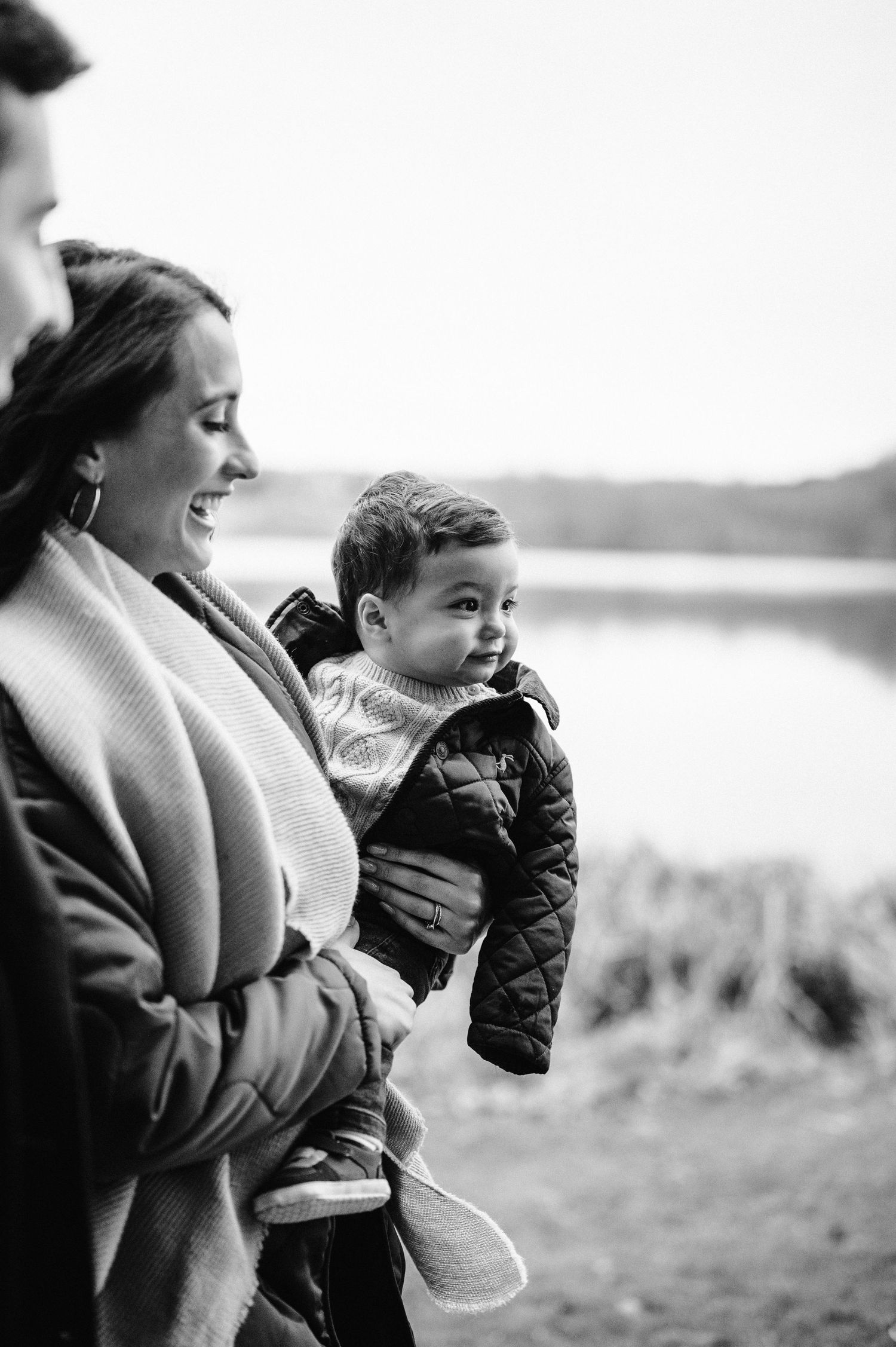 Black and white candid photo of family smiling outdoors near water.