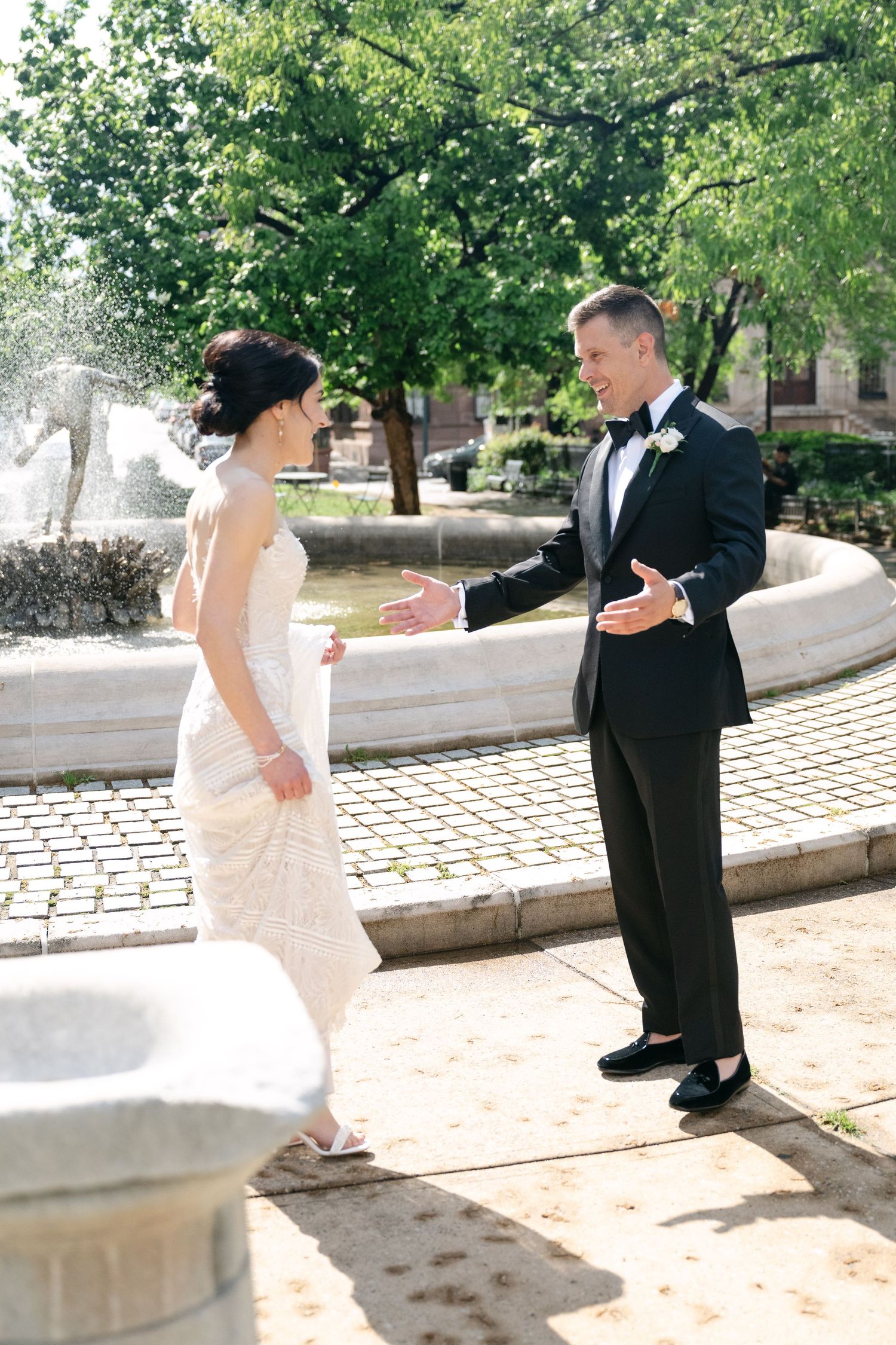 A couple shares their first look moment in formal attire on a cobblestone path surrounded by trees.