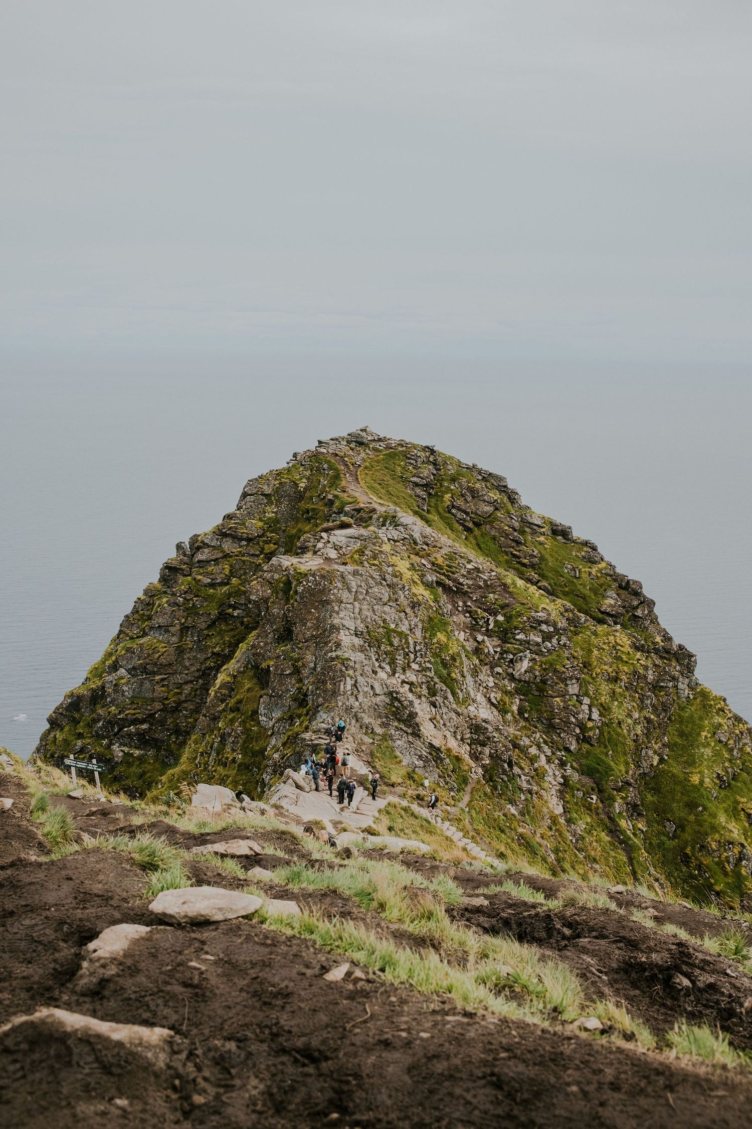 Rocky mountain peak with a narrow hiking trail leading to the summit against a misty backdrop.