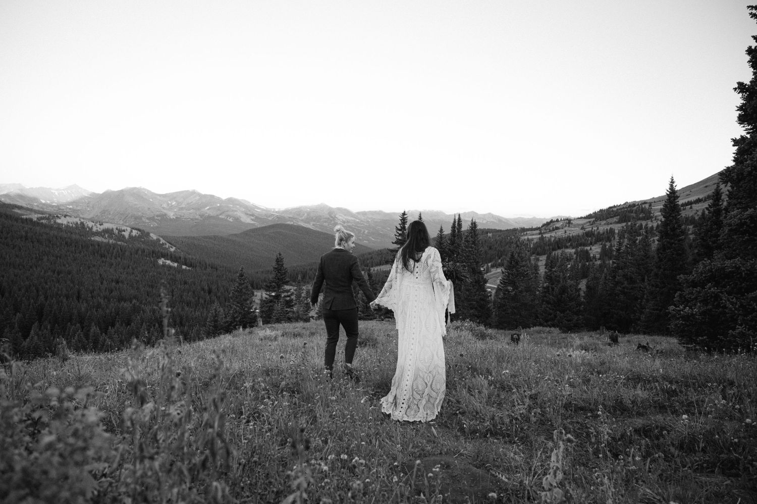Two people walking hand in hand through a mountain meadow in black and white.