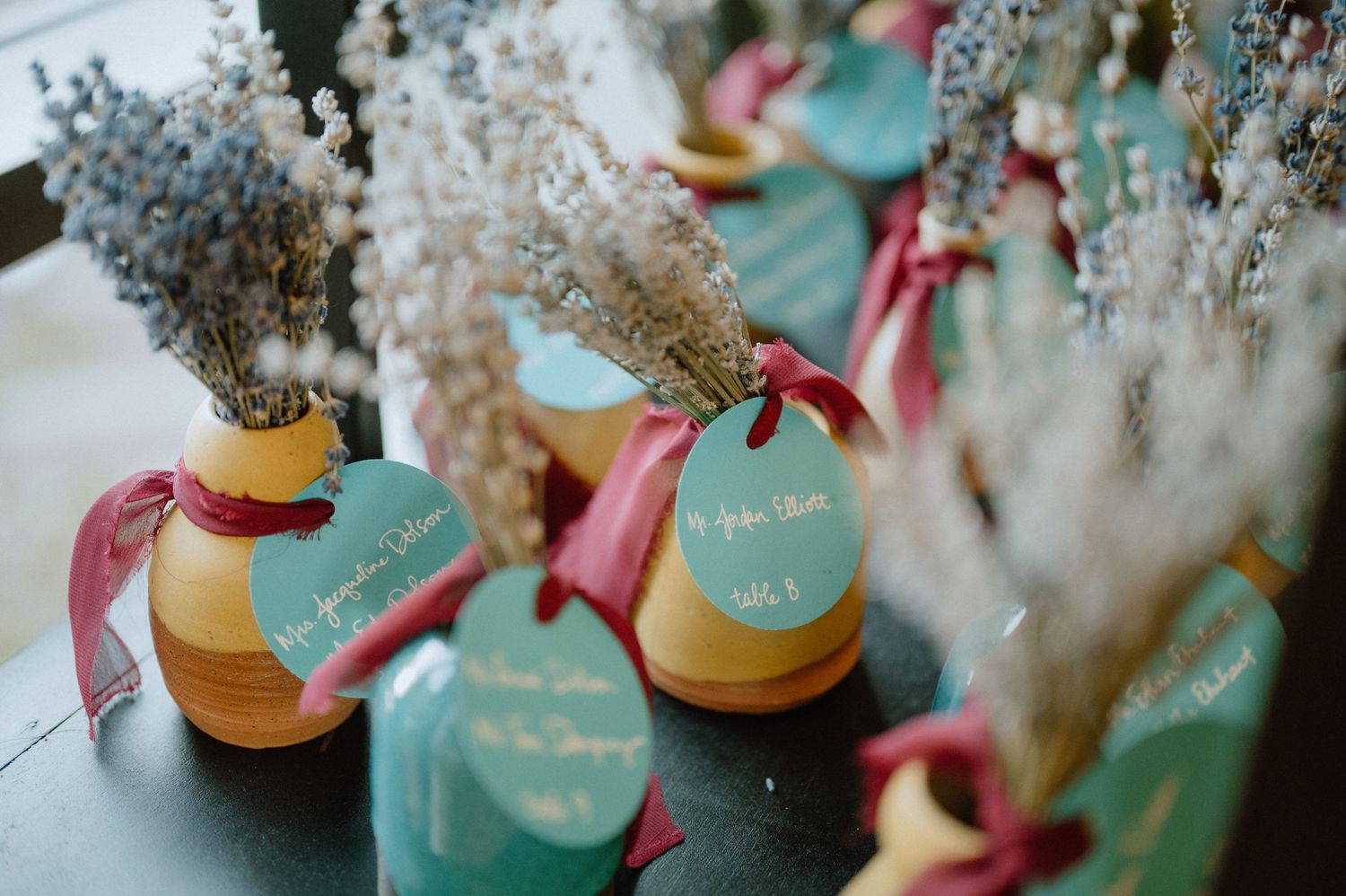Decorative wedding favors in yellow vases with teal tags and dried flowers.