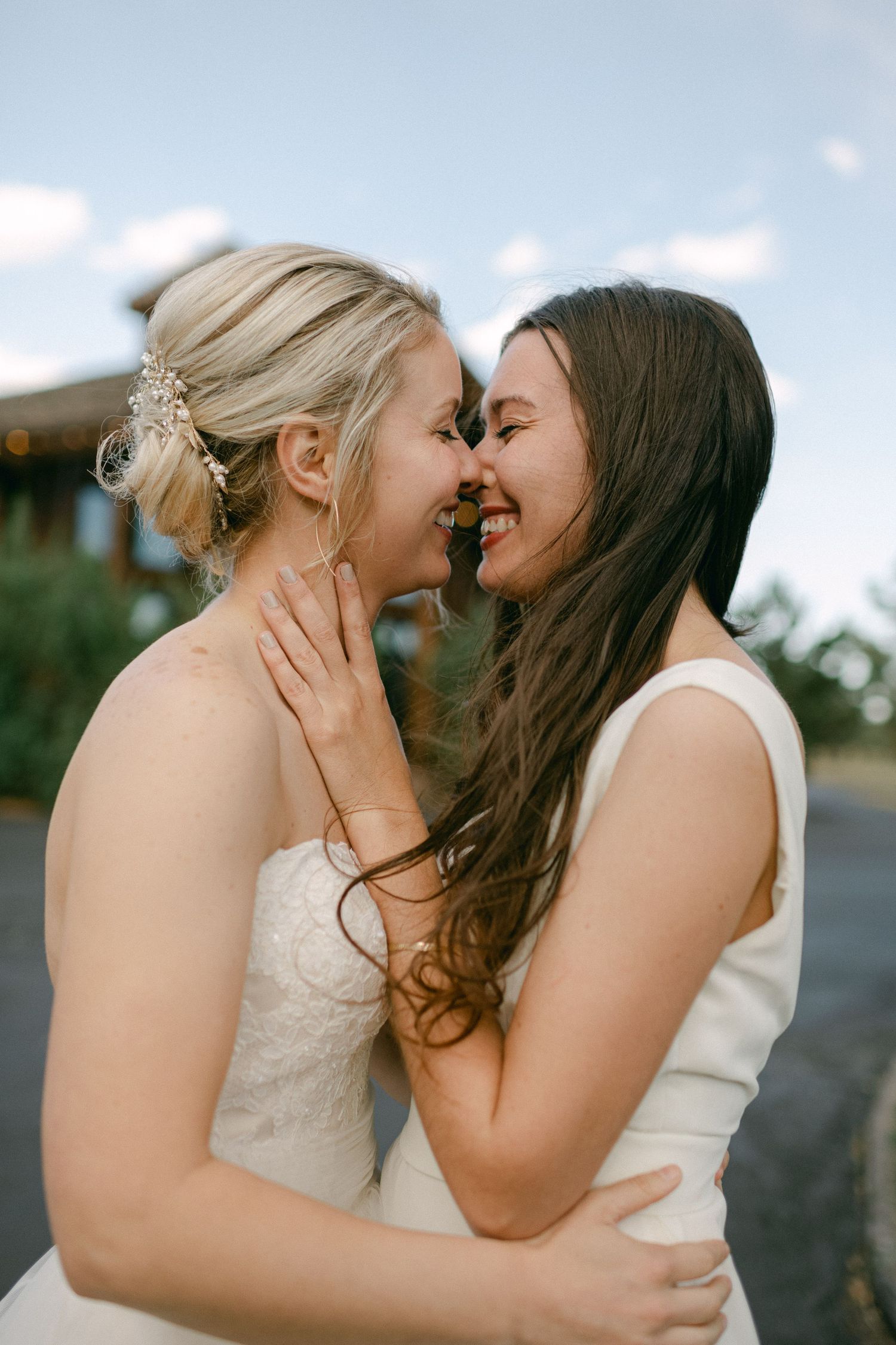 Two people in wedding attire share a tender moment against a blue sky.