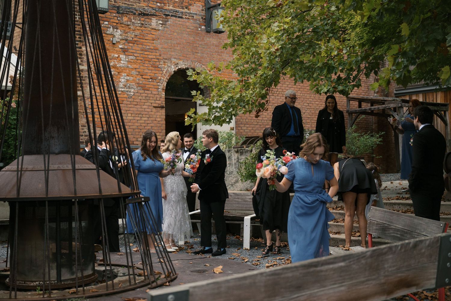 Wedding guests gather outside a rustic brick building during an intimate outdoor ceremony.