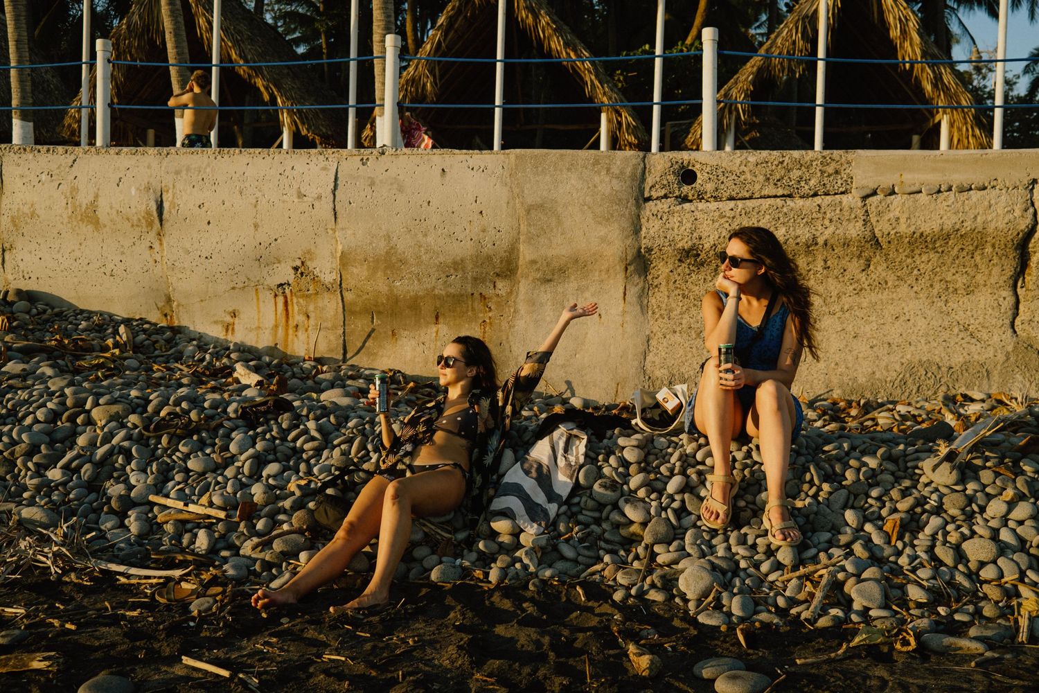People relaxing on a rocky tropical beach at sunset with palm trees.