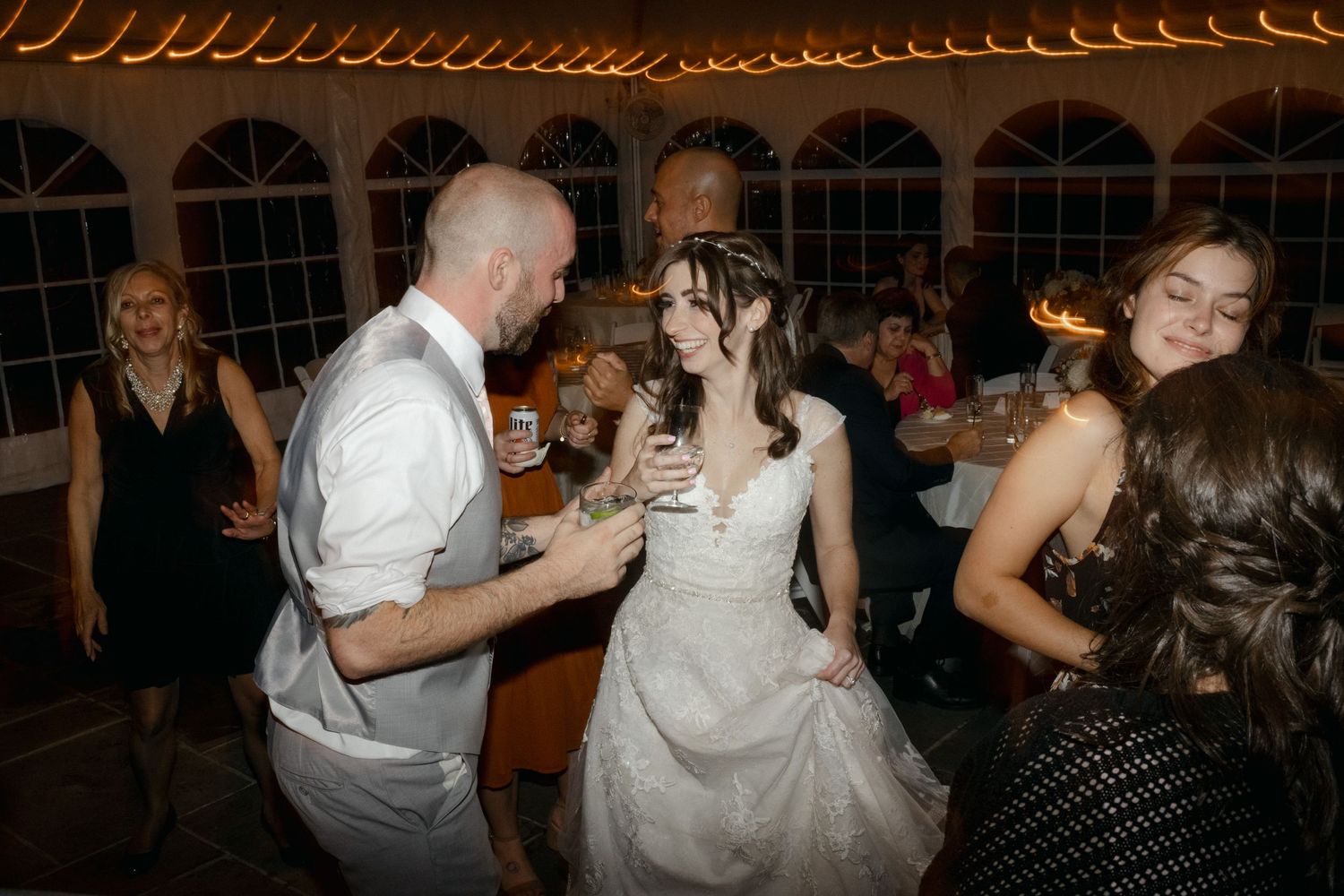 Wedding guests dancing and celebrating on the reception dance floor under string lights.