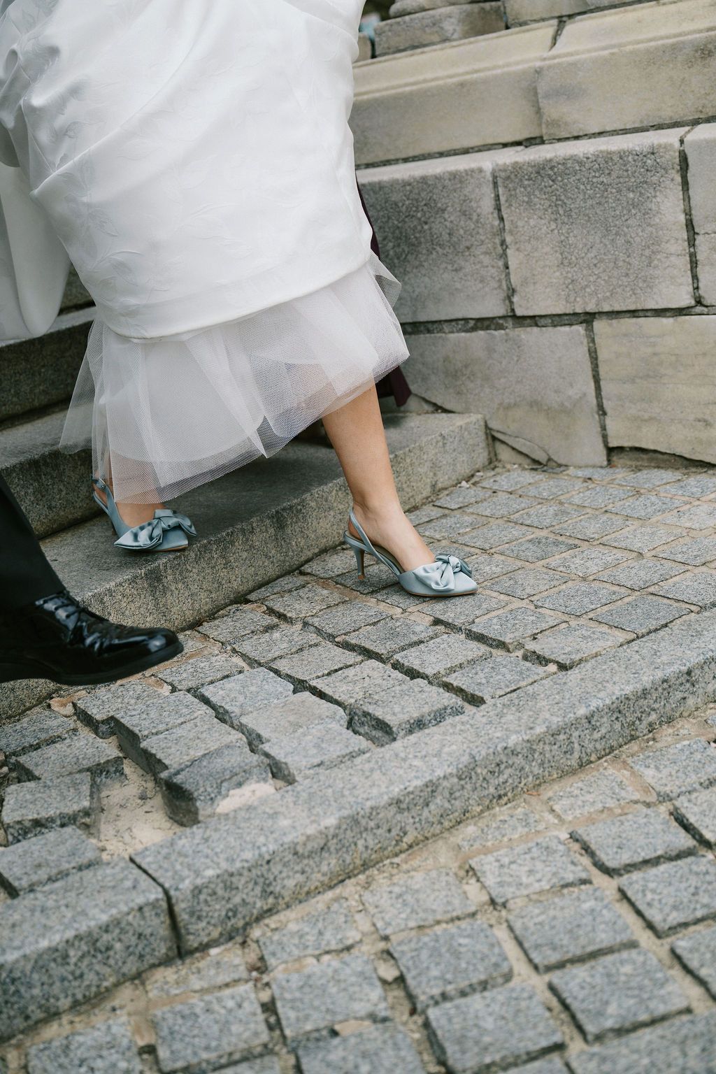 Close-up of bride's sparkly blue shoes and groom's formal shoes on stone steps.