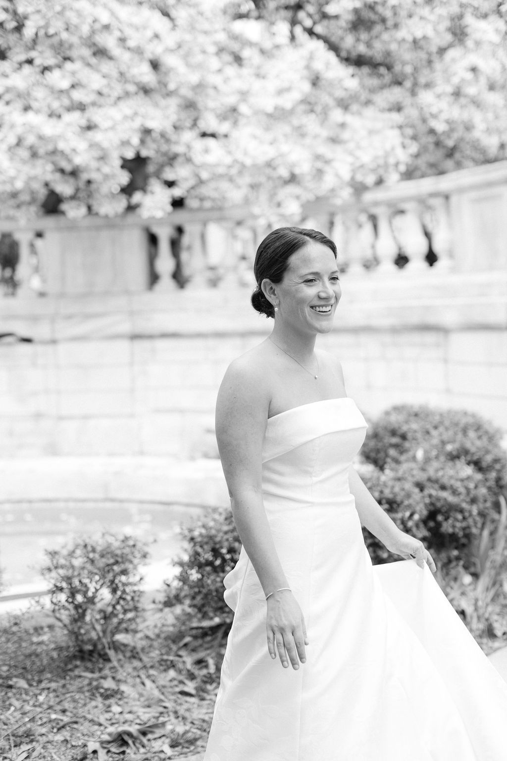 Black and white portraits of a bride in a strapless wedding gown smiling joyfully in an outdoor garden setting.