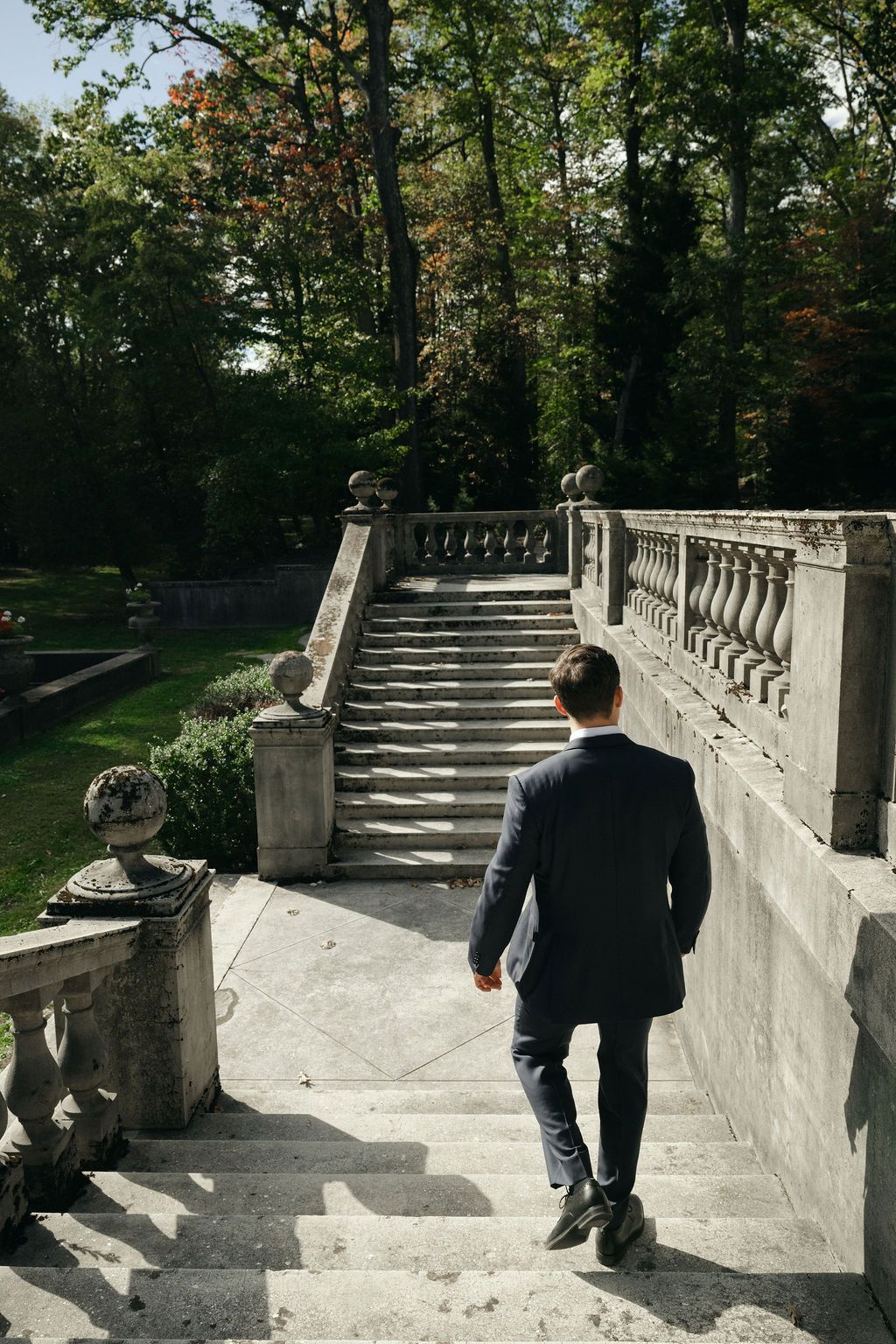 Groom a suit walks along an ornate stone staircase in a garden setting at Strong Mansion on Sugarloaf Mountain