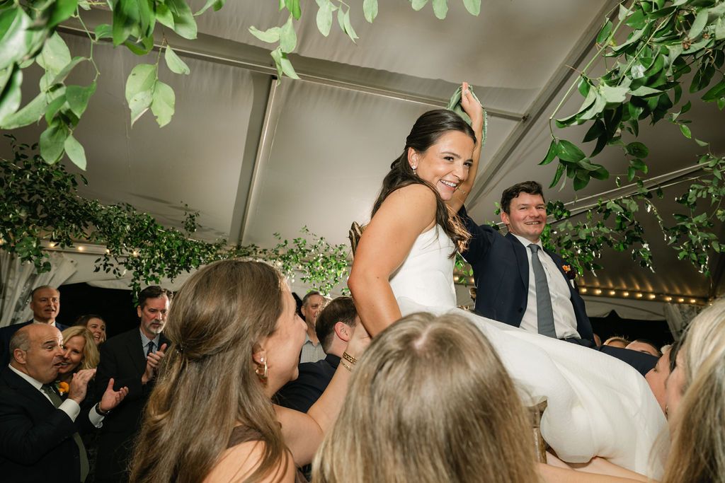 Wedding guests lift and celebrate during a lively dance party under a tent with string lights at Strong Mansion on Sugarloaf Mountain