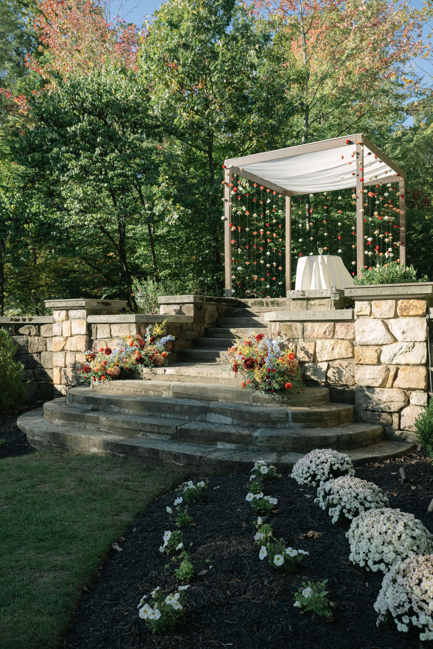 Outdoor wedding ceremony space with white canopy and stone steps decorated with white flowers.