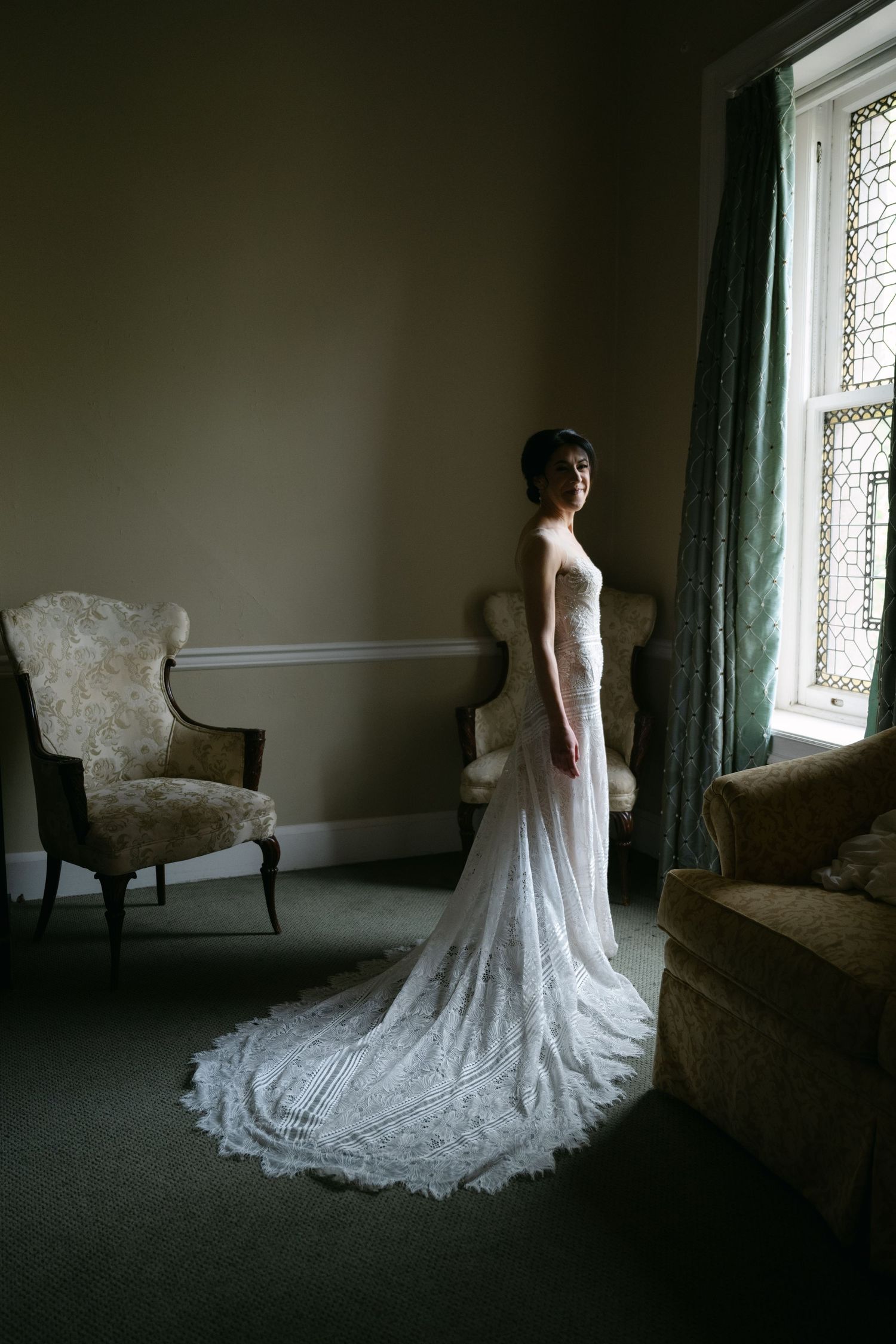 An elegant wedding dress with a long lace train photographed in a moody room with vintage furniture at a Baltimore engineers club wedding