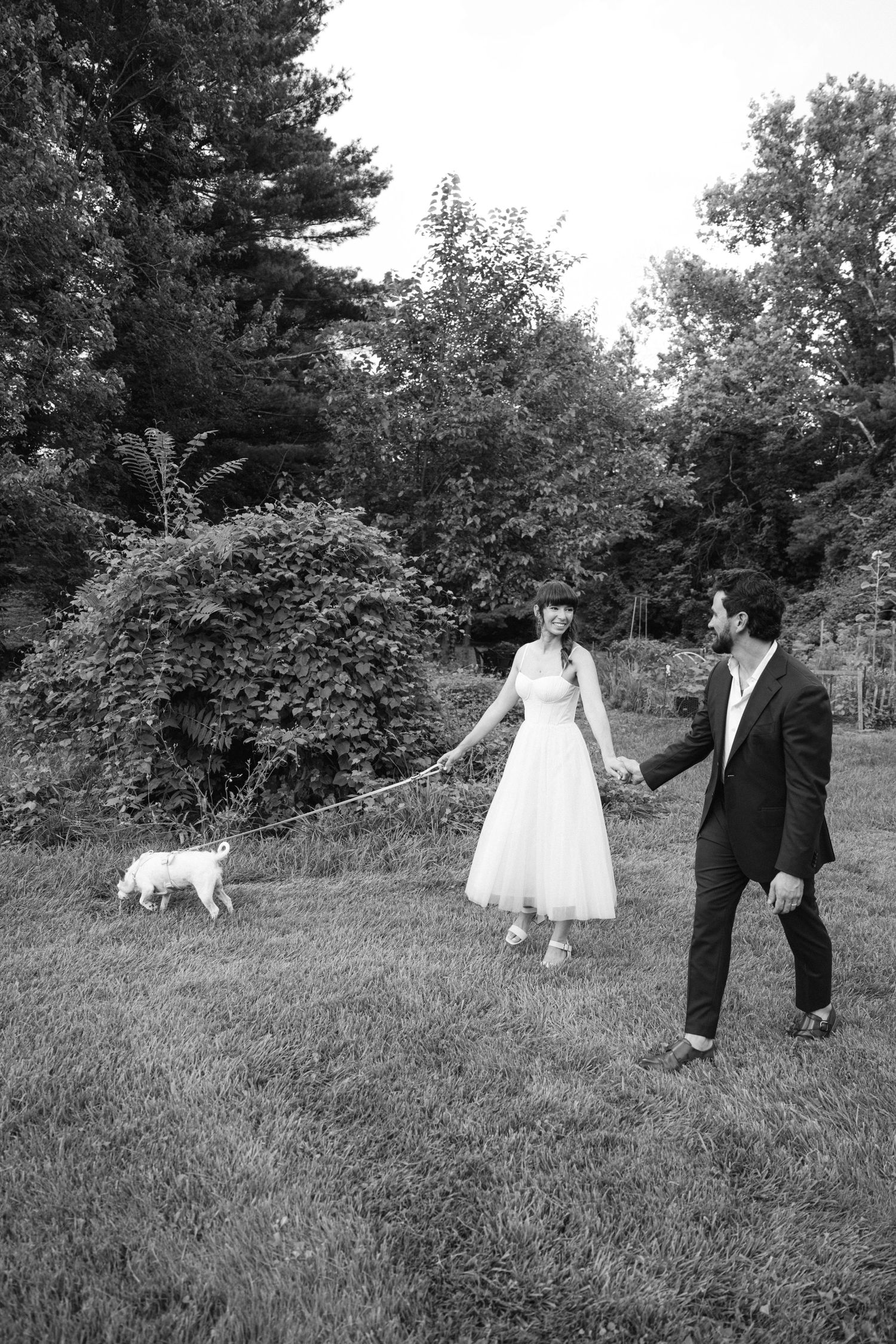 Wedding couple playfully running through a grassy field with trees in the background.