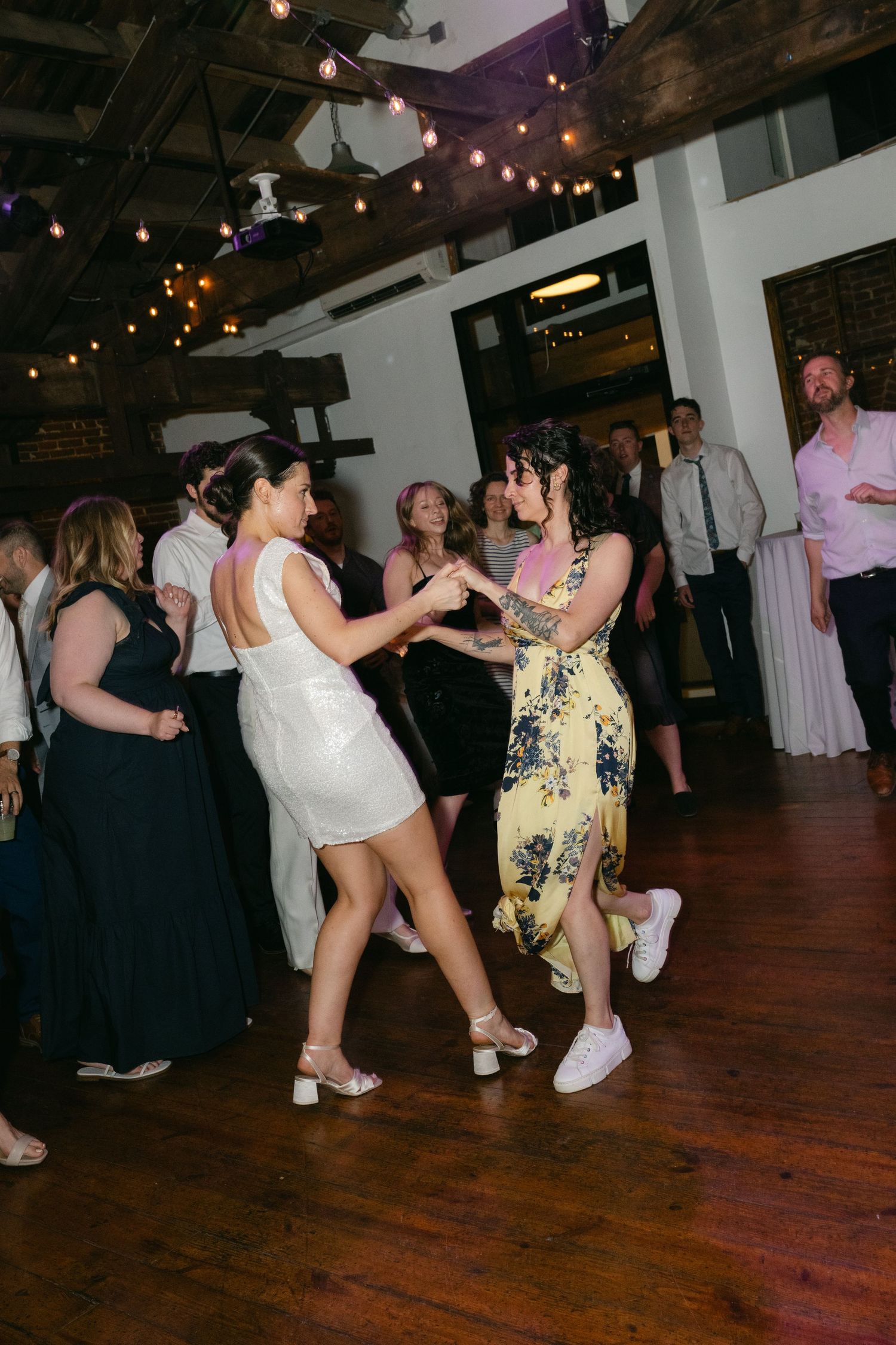 People dancing together at a party venue with string lights and exposed brick walls.
