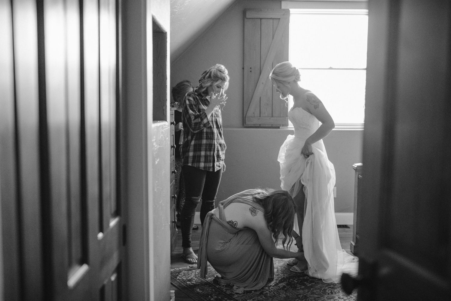 A candid black and white photo shows wedding preparations in a sunlit room.