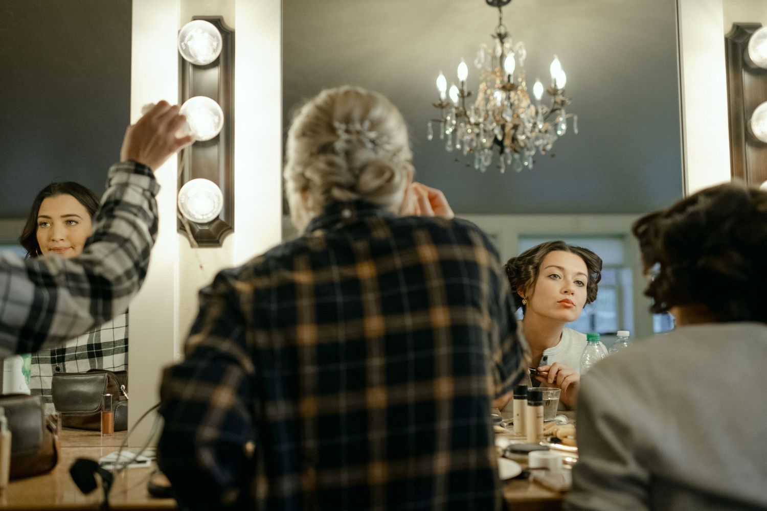 Wedding preparation scene in elegant dressing room with chandelier and vanity mirrors.
