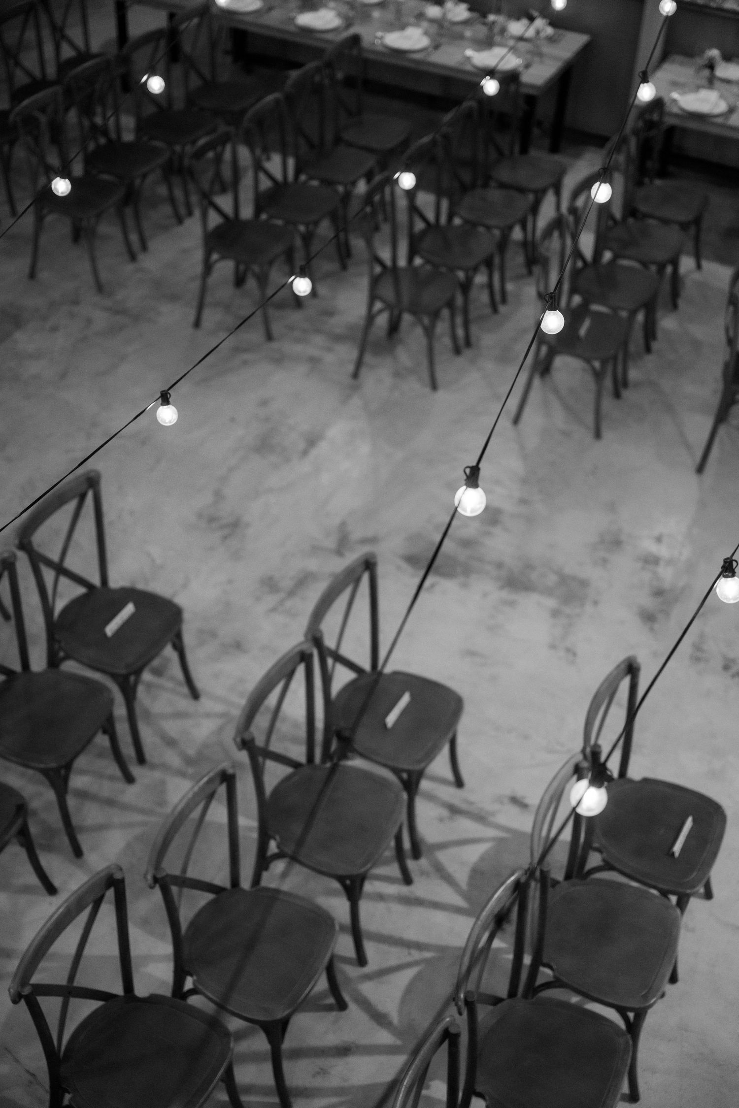 Empty black chairs arranged in rows with hanging string lights creating moody atmosphere.