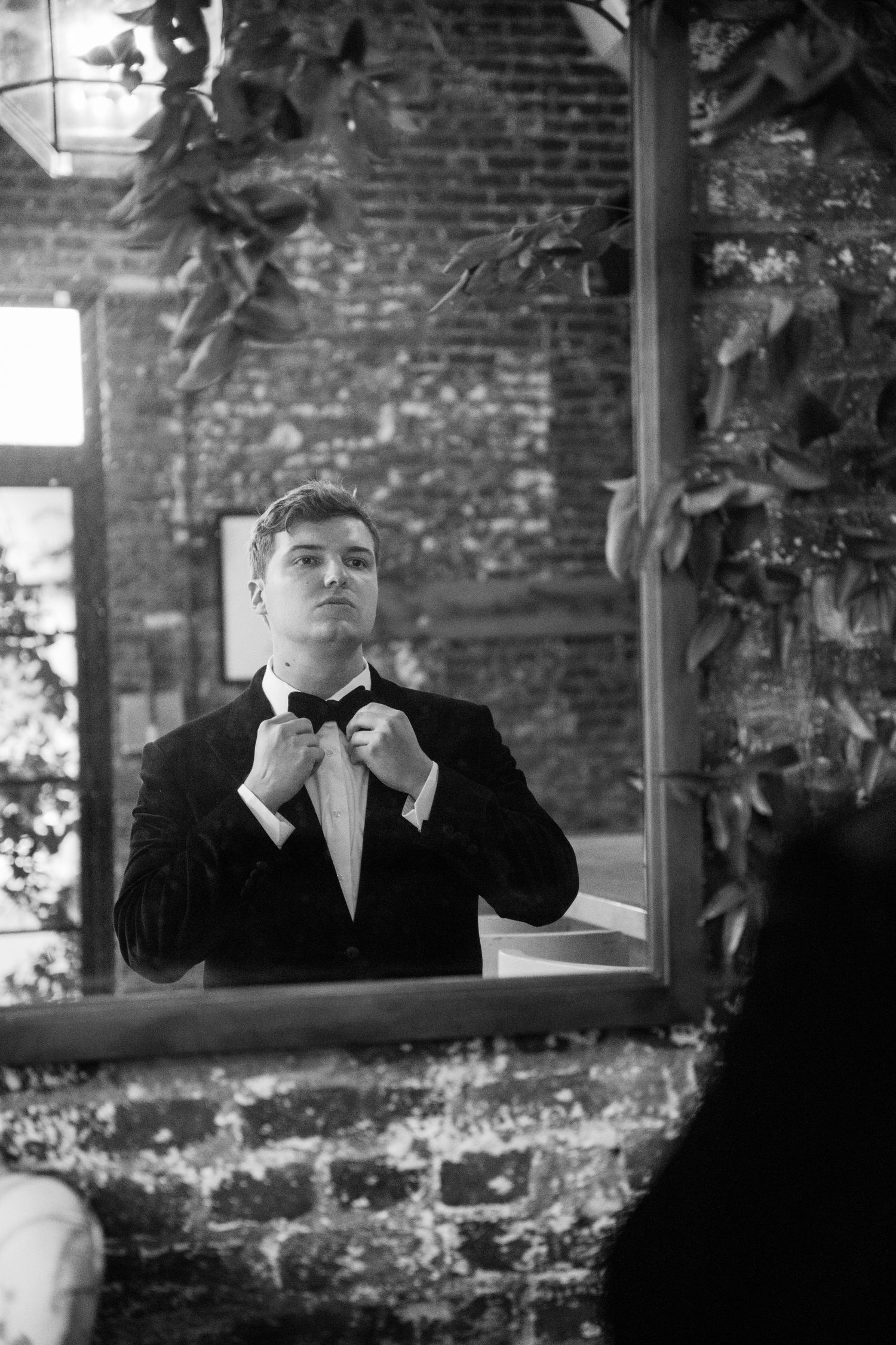 Black and white portrait of formal attire adjustments in front of rustic brick wall.
