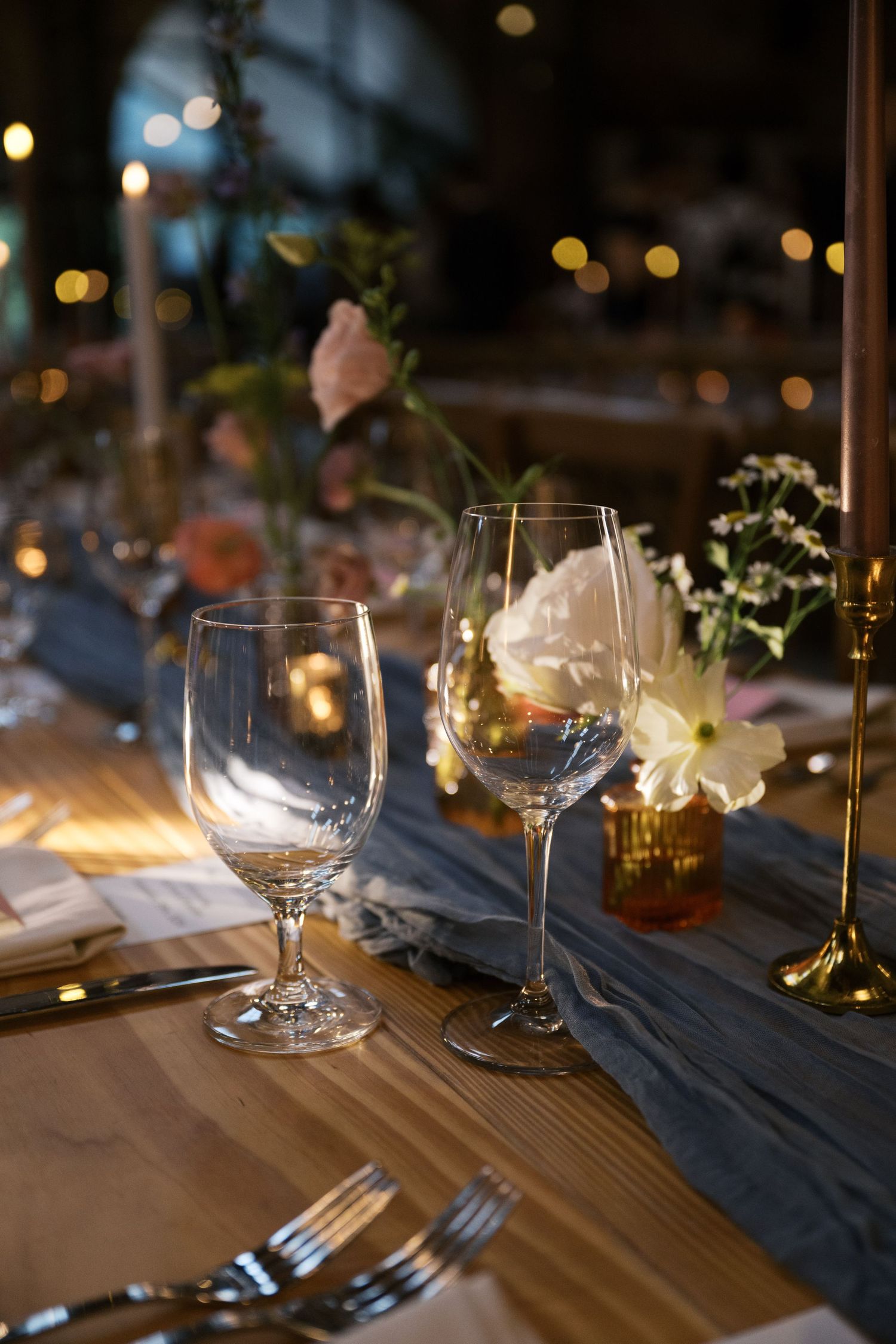 Wine glasses and place settings on wooden table with moody evening lighting and floral accents.