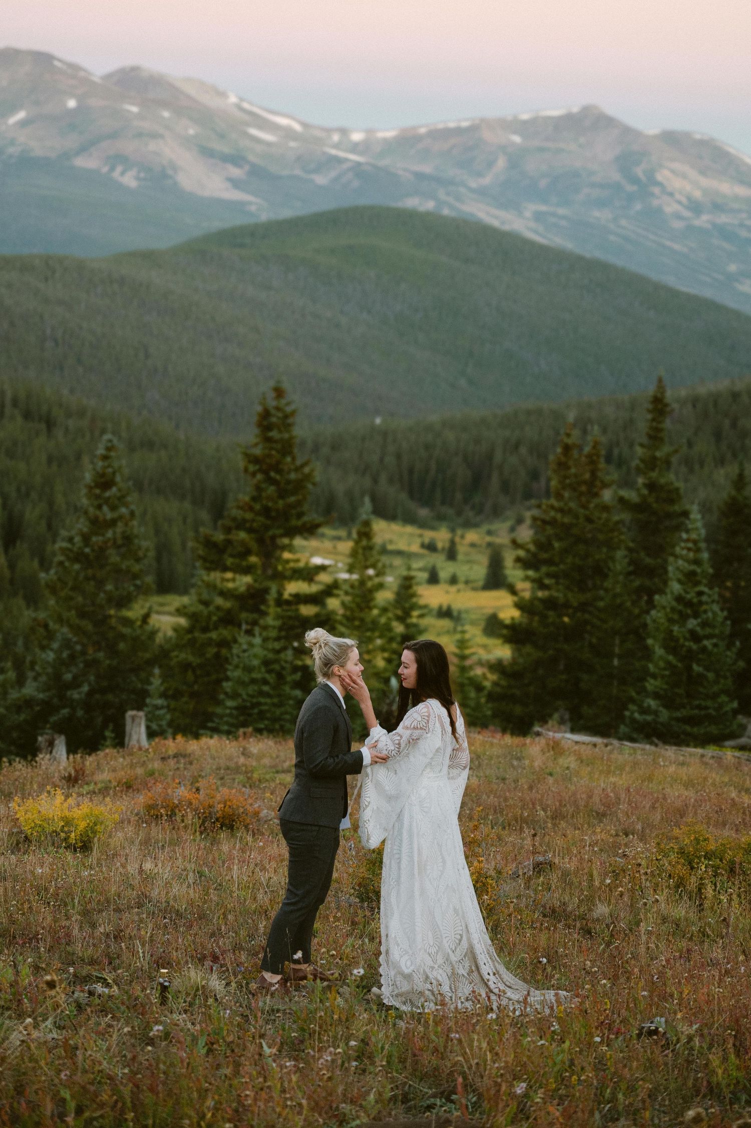Breathtaking mountain sunset provides backdrop for couple in formal attire on alpine meadow.