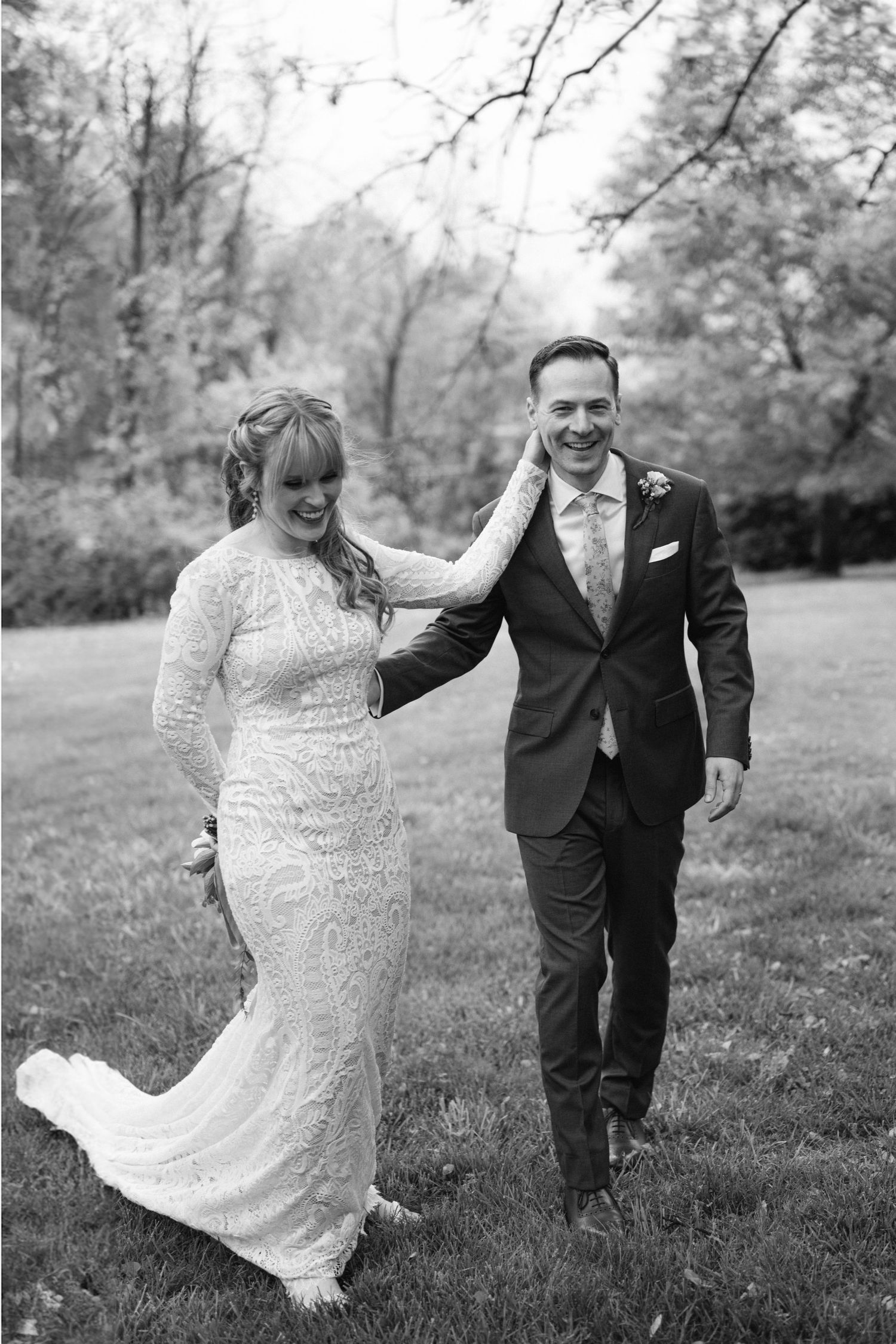 A joyful couple sharing a candid moment together outdoors in their wedding attire on a grassy lawn.