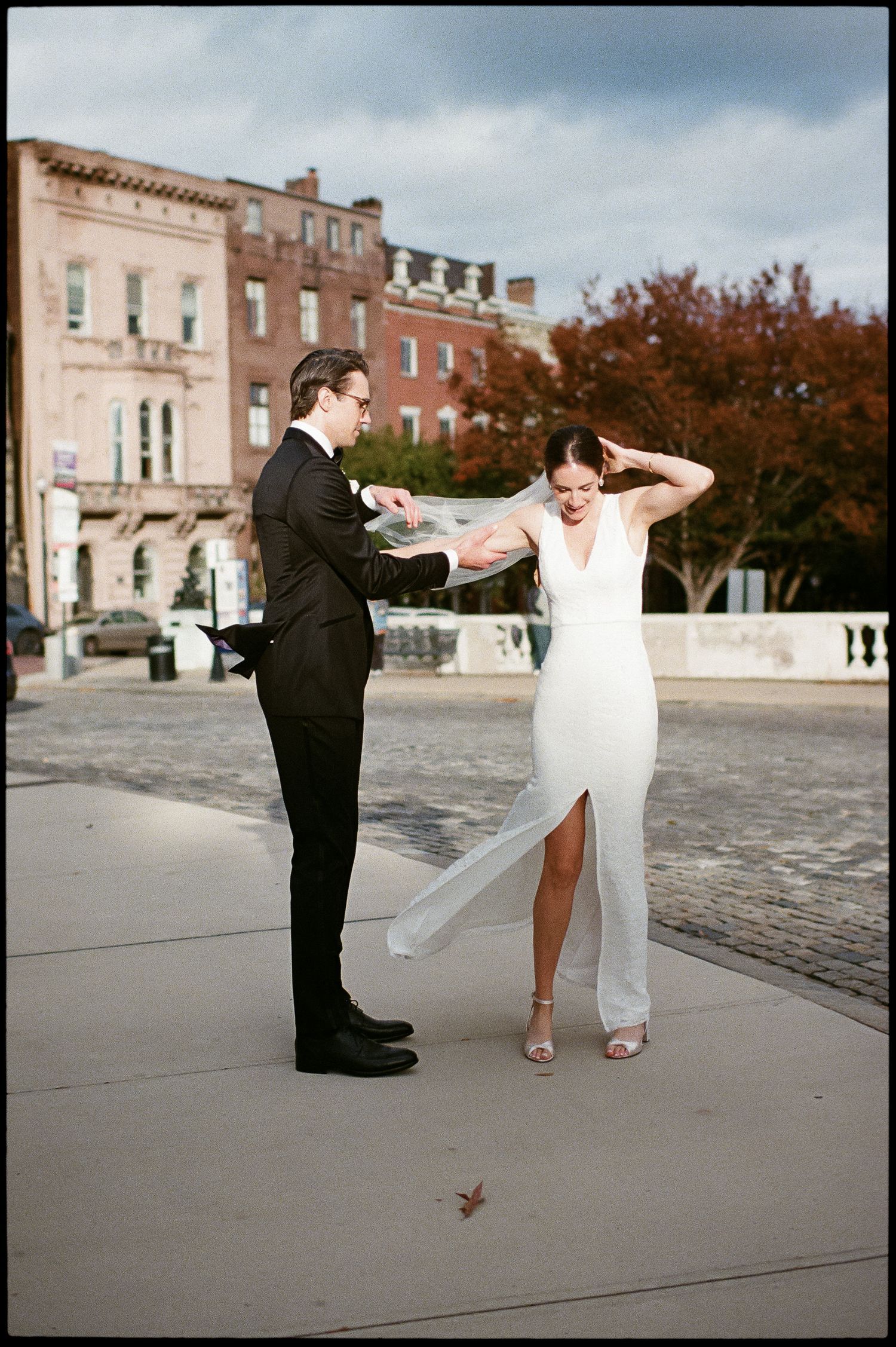 A bride and groom share a playful moment outside historic brick buildings.