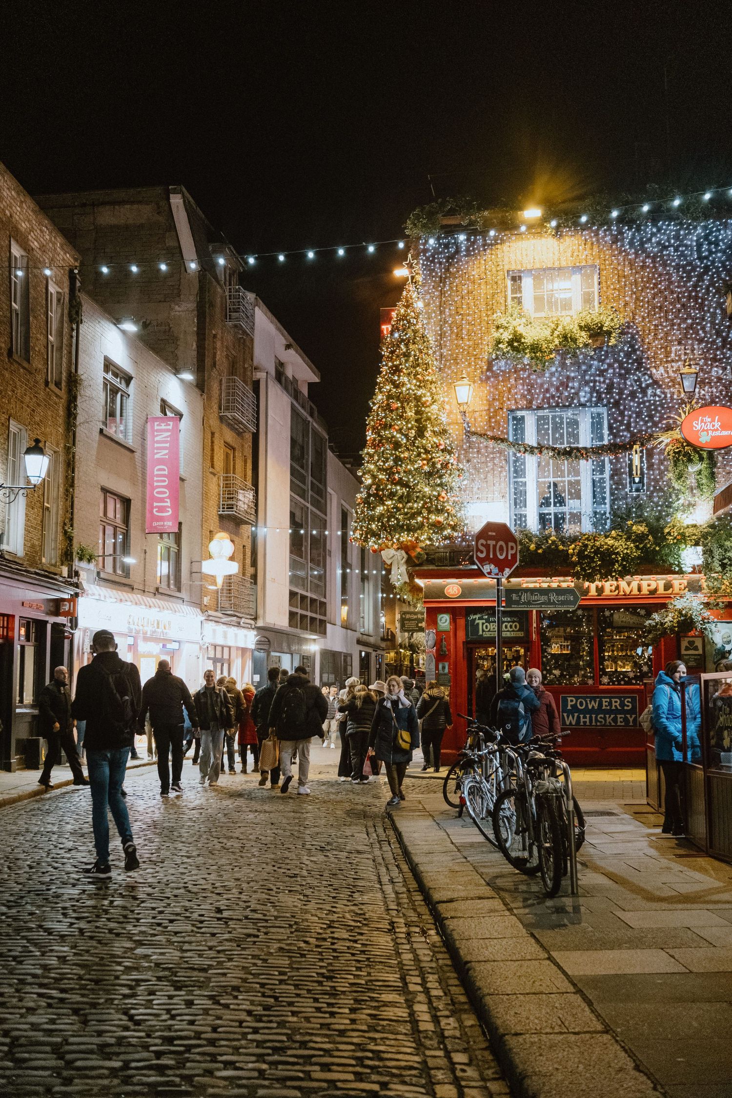 Festive Christmas street scene with illuminated decorations and cobblestone pathway.