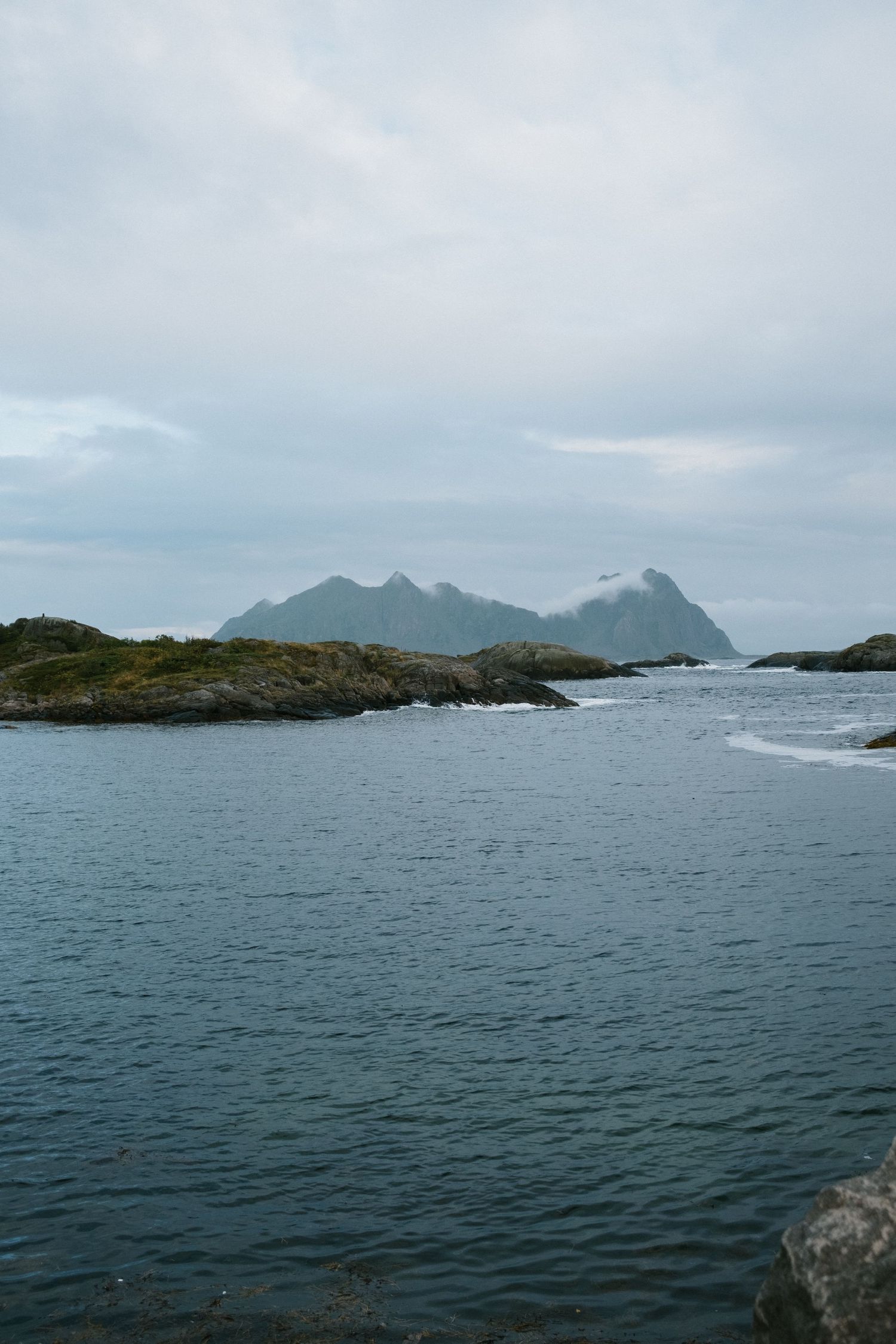 Rocky coastline with jagged mountain peaks rising from the sea under cloudy skies.