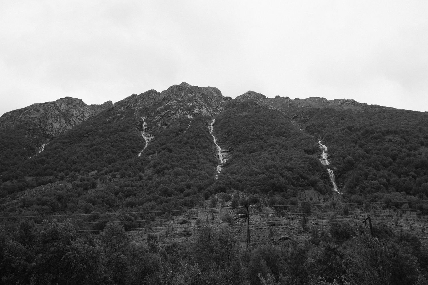 Black and white mountain landscape showing multiple waterfalls streaming down rocky slopes.
