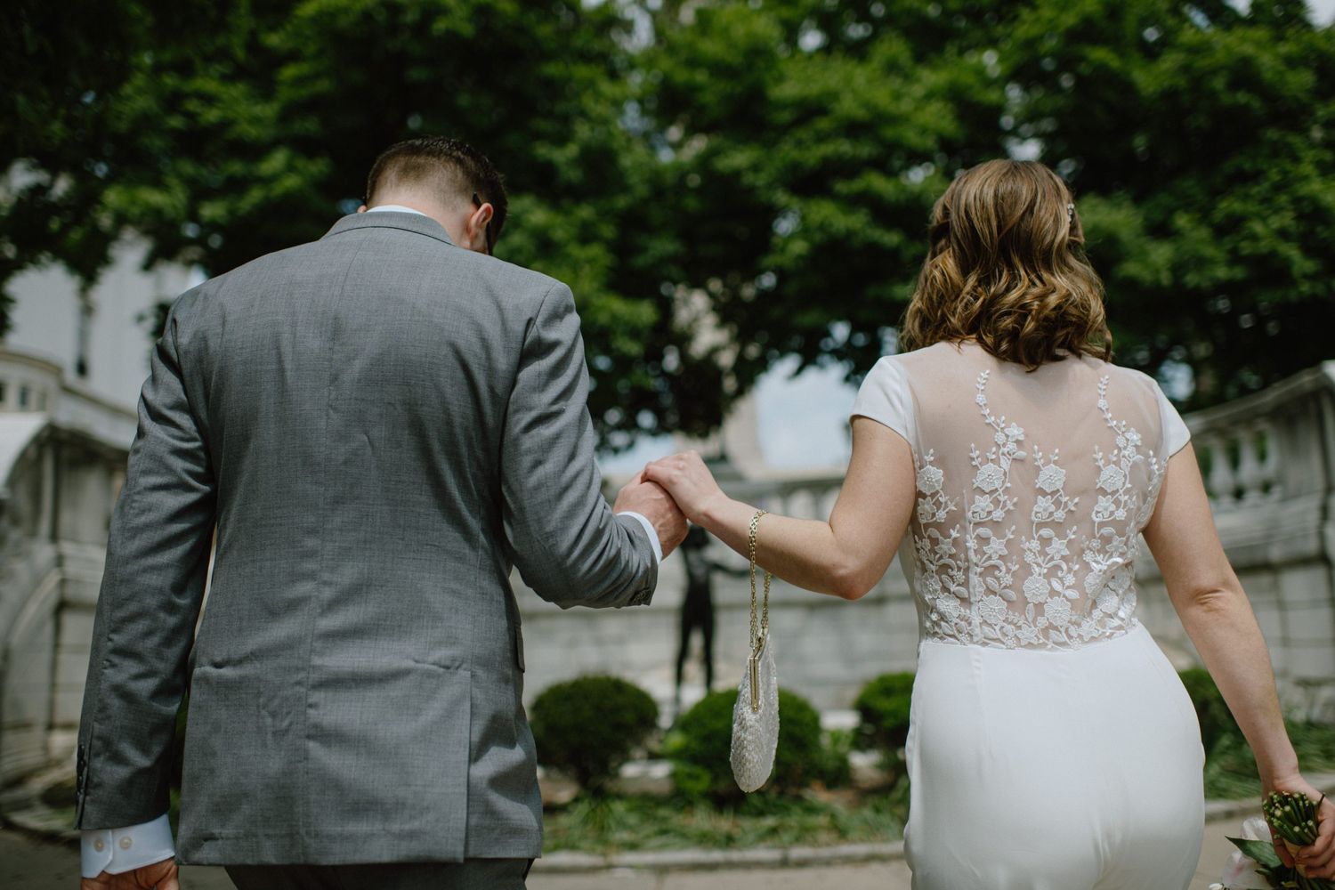 Couple in wedding attire walking hand in hand viewed from behind.