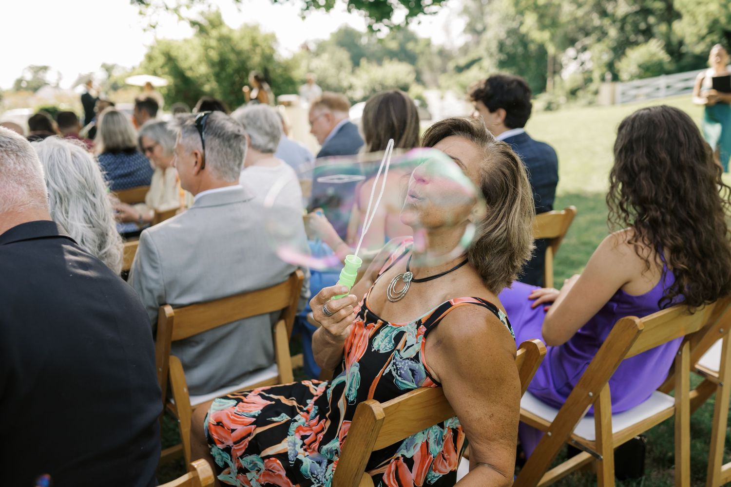Wedding guests enjoying the outdoor ceremony while seated in wooden folding chairs.