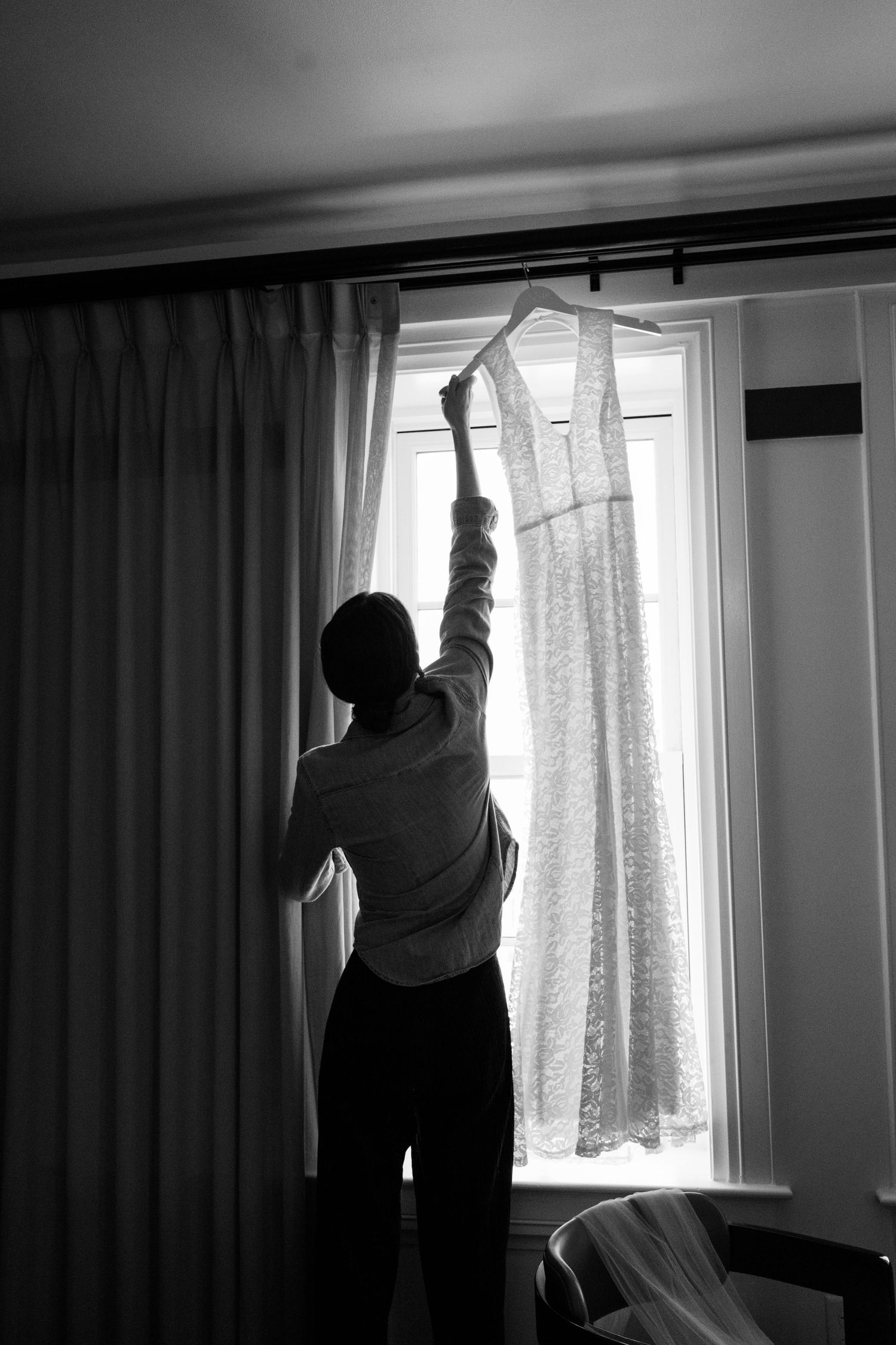 Silhouetted figure reaching up to adjust curtains in a sunlit window.