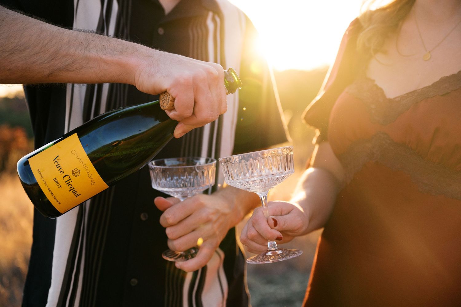 Someone pouring champagne into vintage glasses during golden hour outdoors.