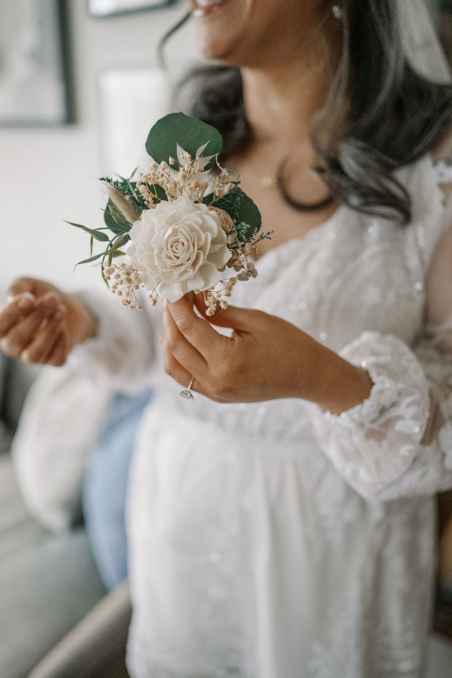 Someone wearing a white lace robe holds a delicate cream rose bouquet with eucalyptus leaves and baby's breath.