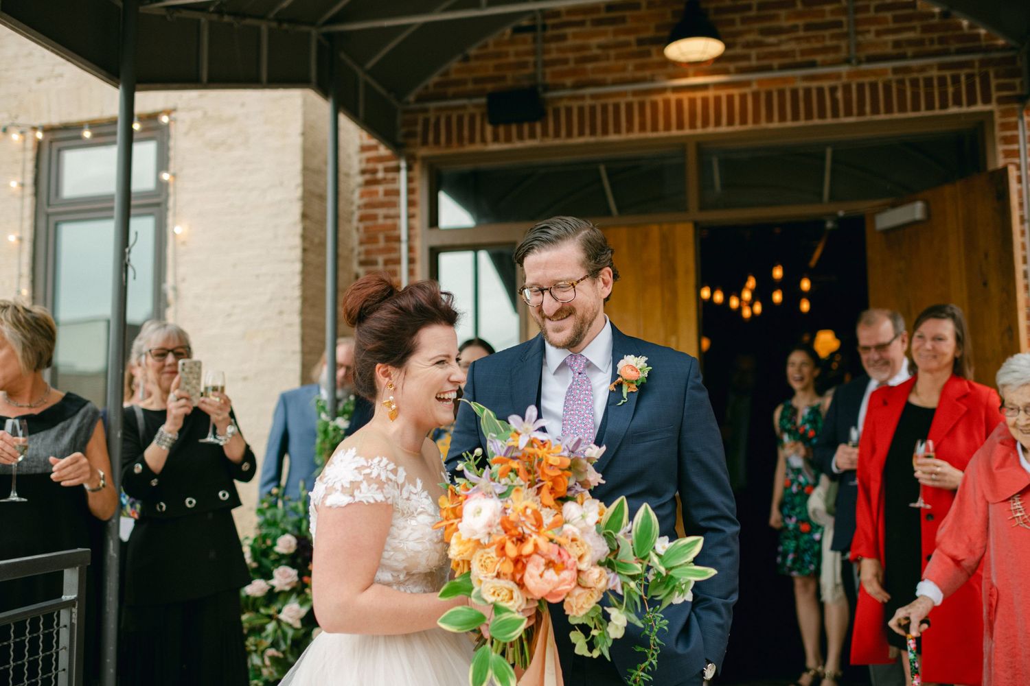 Wedding celebration with guests applauding outside a brick venue entrance.
