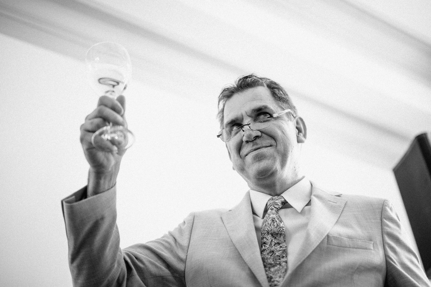 Man in light suit raising a toast glass during formal event.