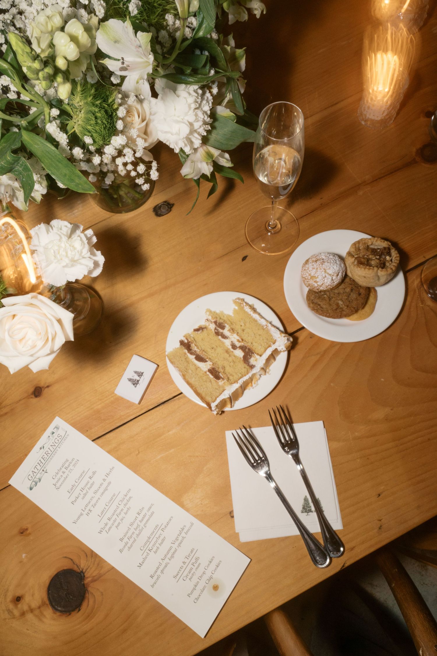 Wedding reception table setting with floral centerpiece, cake slice, and menu card on wooden surface.