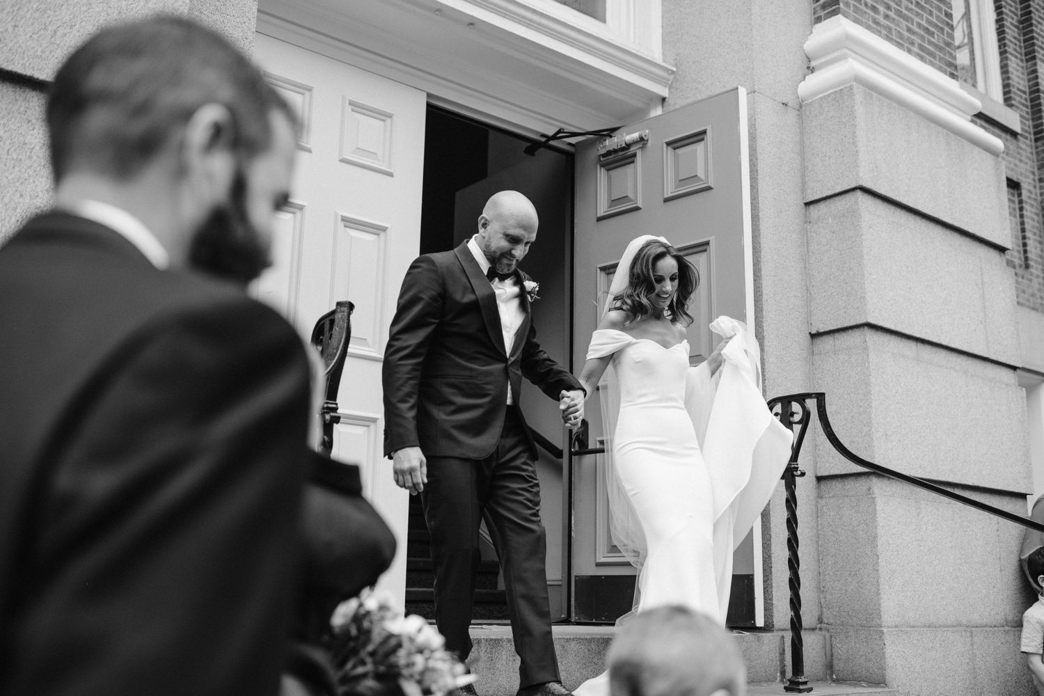 A joyful couple descends the steps of a historic building during their wedding celebration.