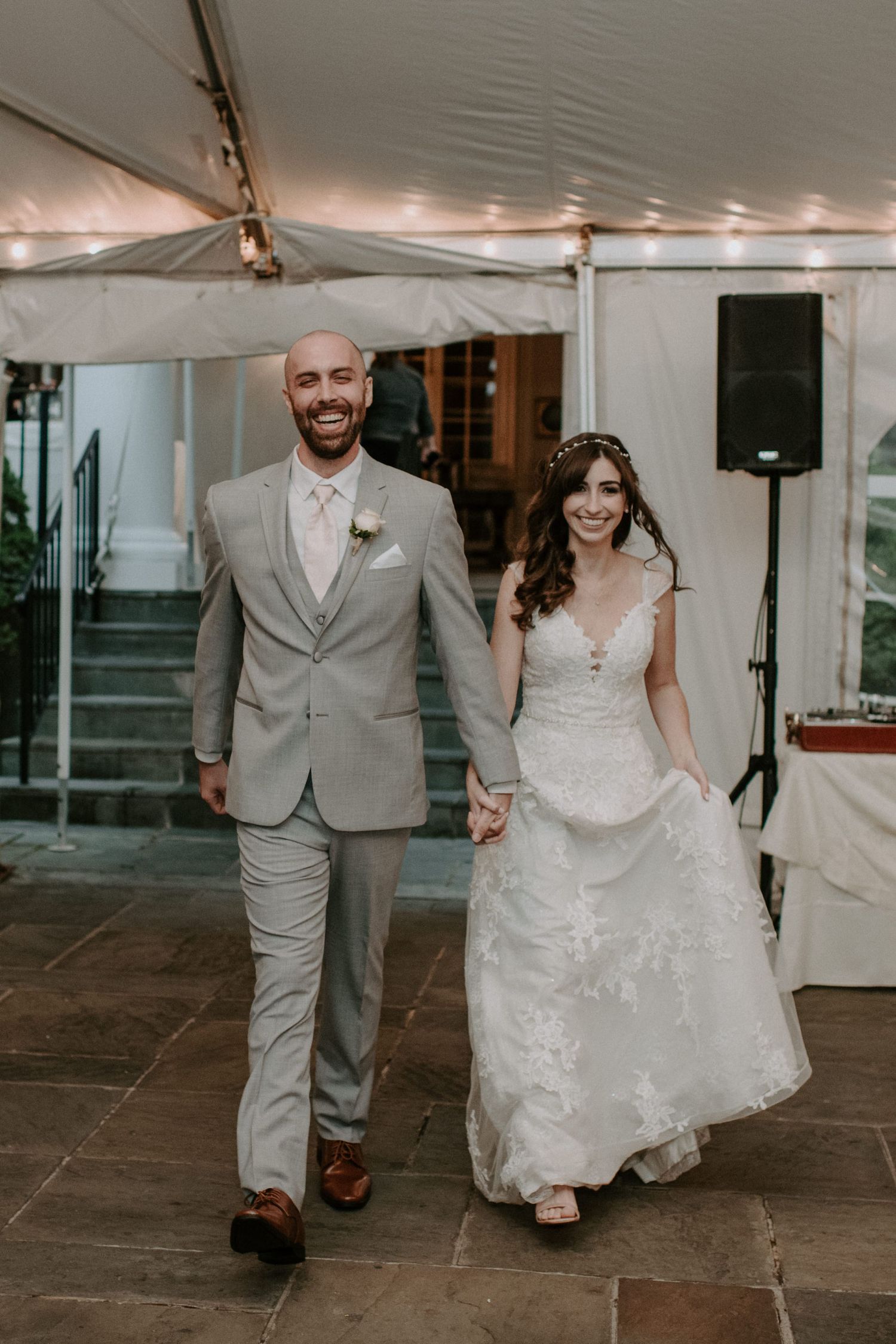 Newlyweds walking together under a white tent reception space.