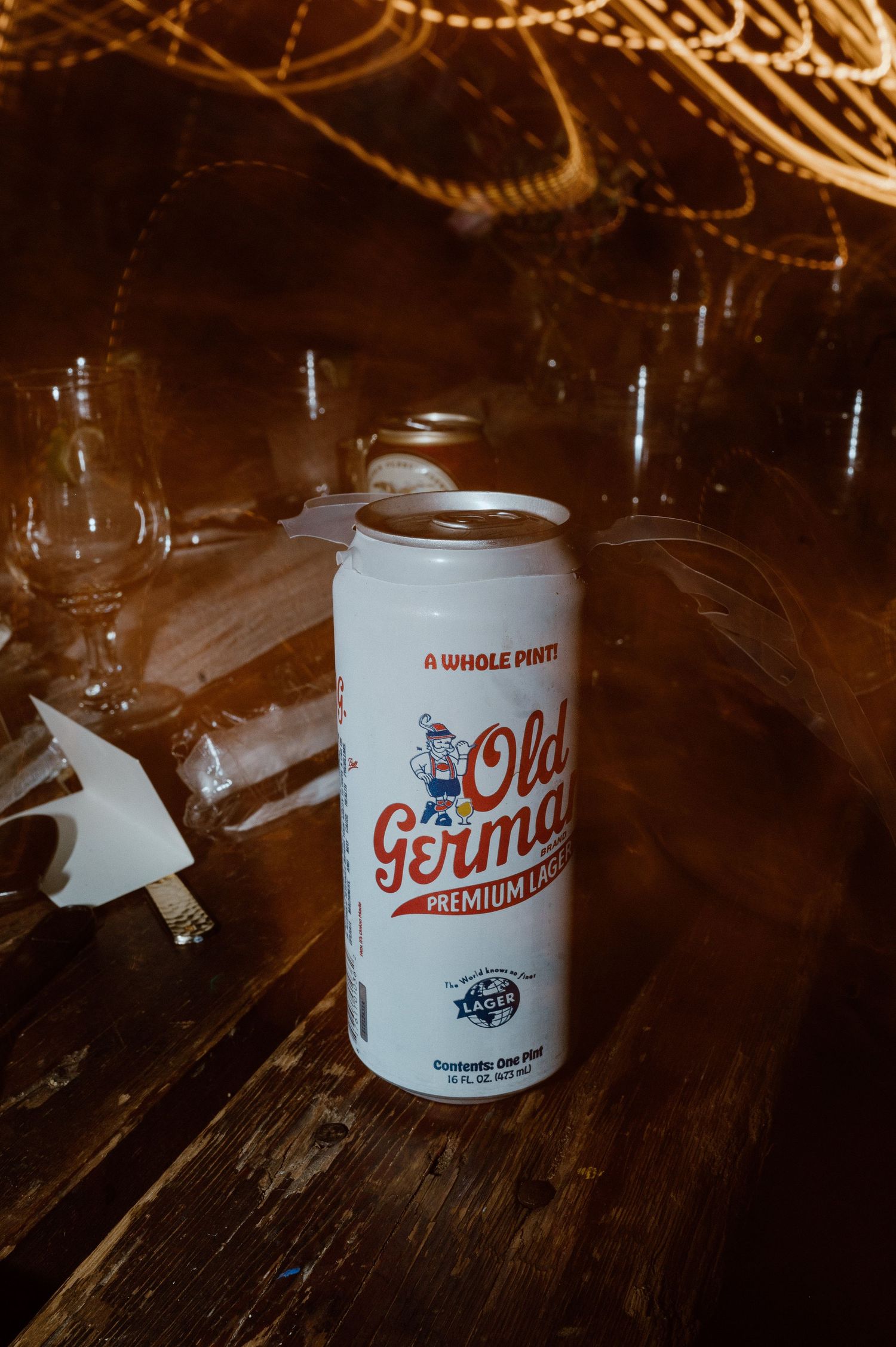 Can of Old German Premium beer on wooden table with party lights in background.