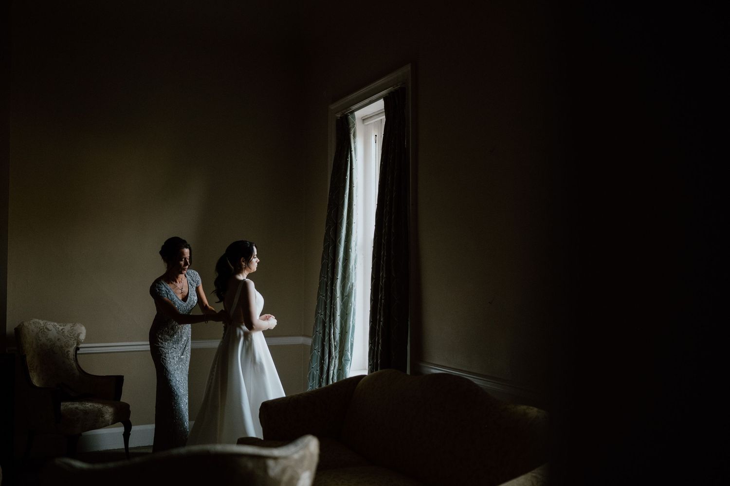 Silhouetted figures by window in dark room with dramatic lighting.