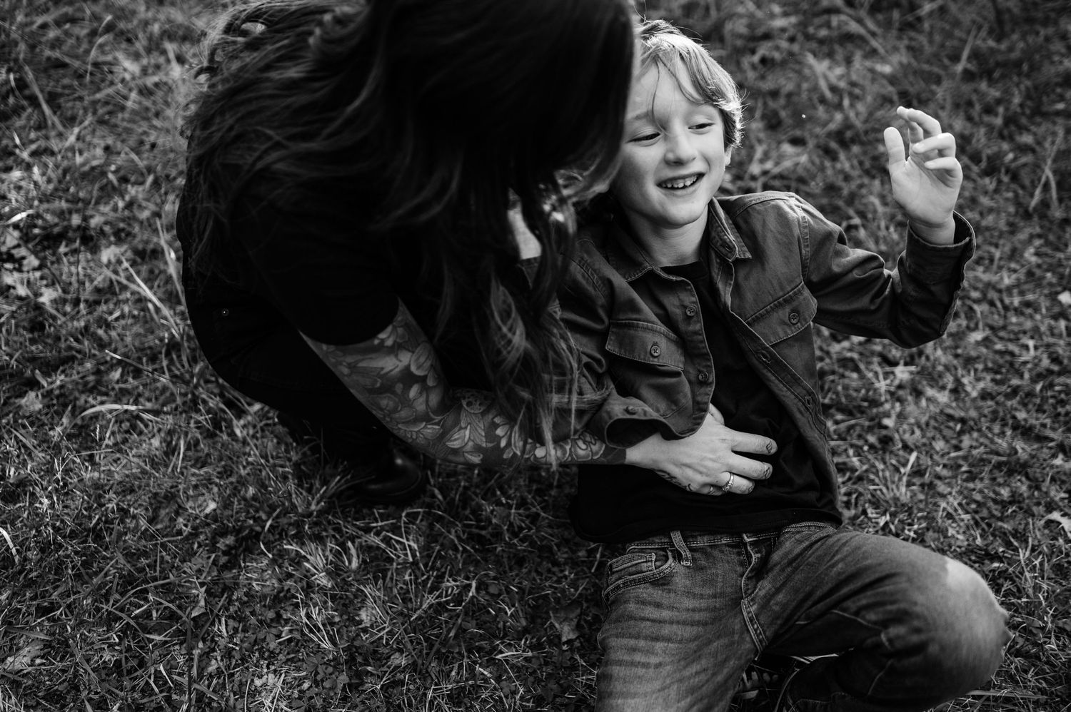 A candid black and white photograph capturing laughter and playfulness on the grass.