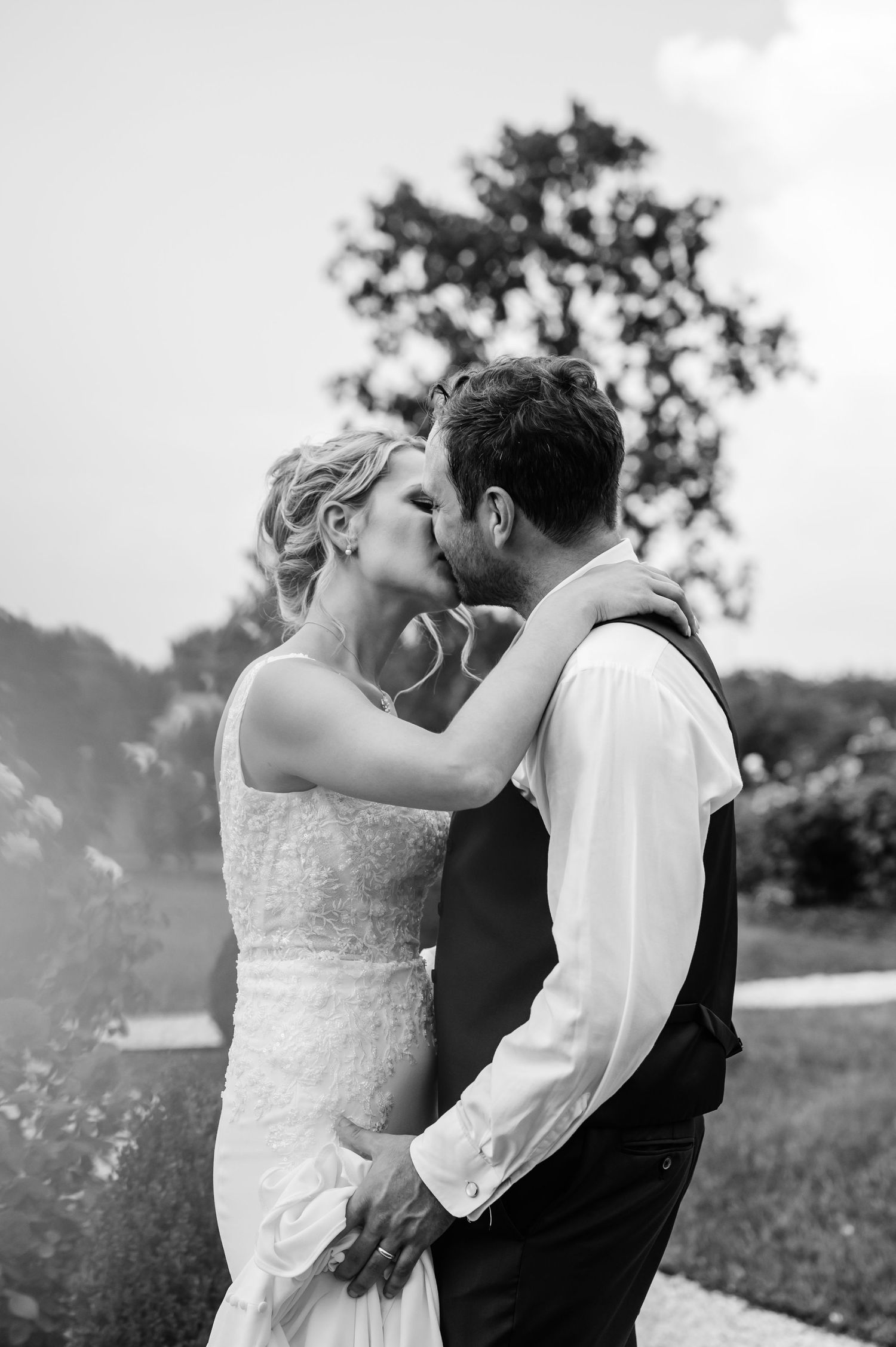 A romantic black and white portrait of newlyweds sharing a kiss in a sunlit field.