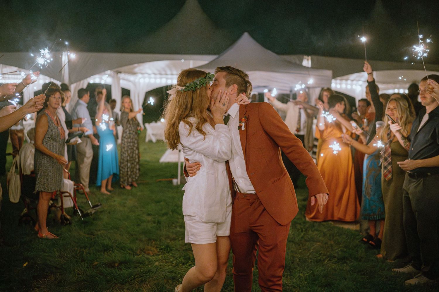 Newlyweds walk through sparkler tunnel during wedding reception at outdoor evening celebration.