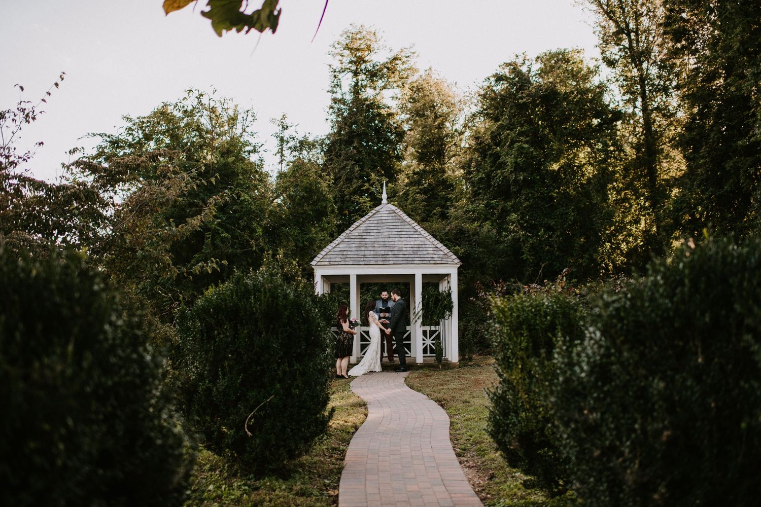 White garden gazebo with pathway surrounded by trees at dusk.